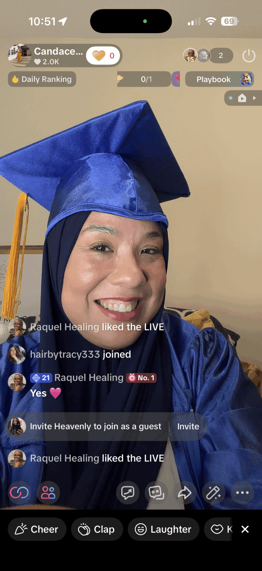 Woman in blue graduation cap and gown smiling, wearing a hijab, indoors.