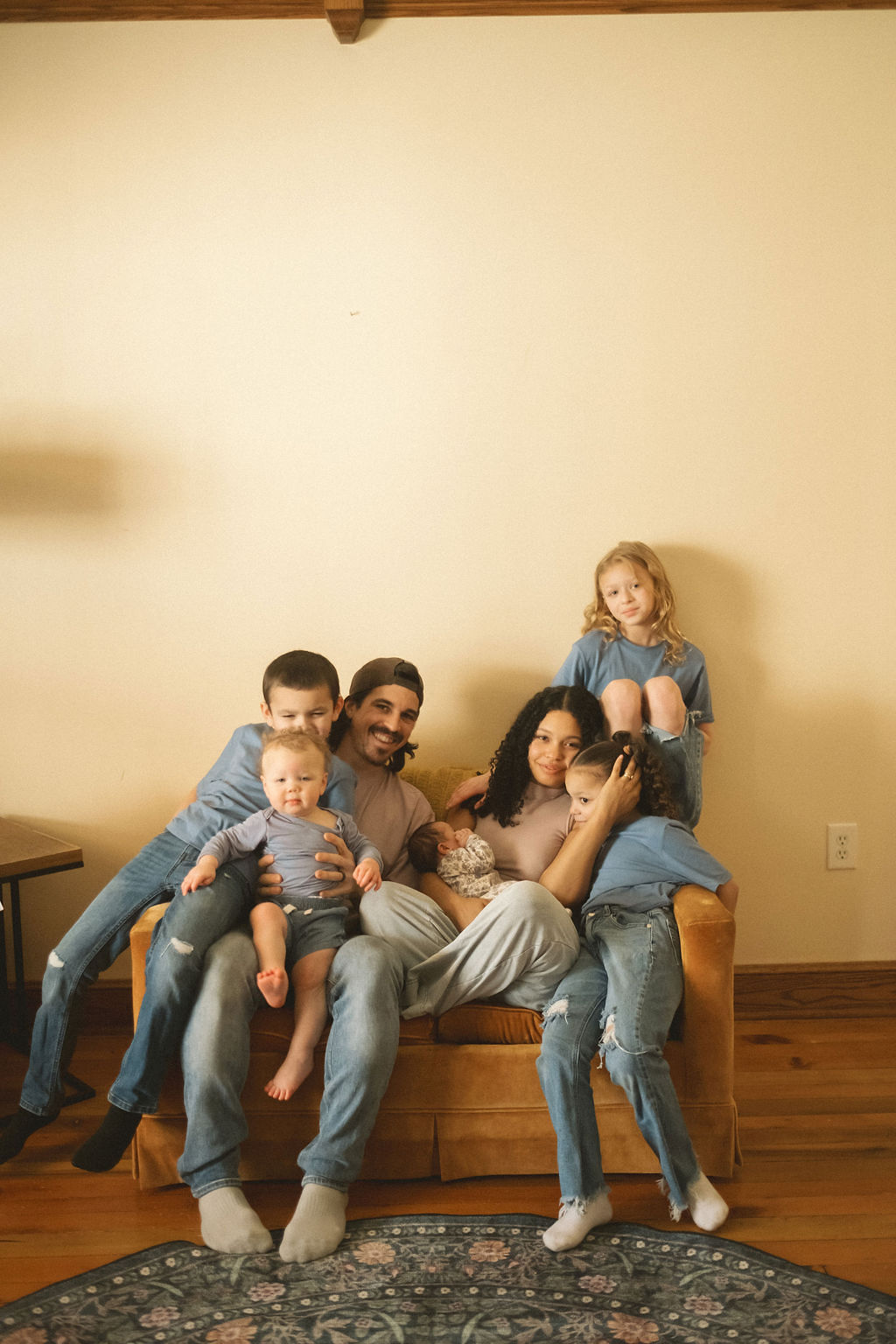 Group of five people sitting on a sofa in a living room, with a plain wall behind them.
