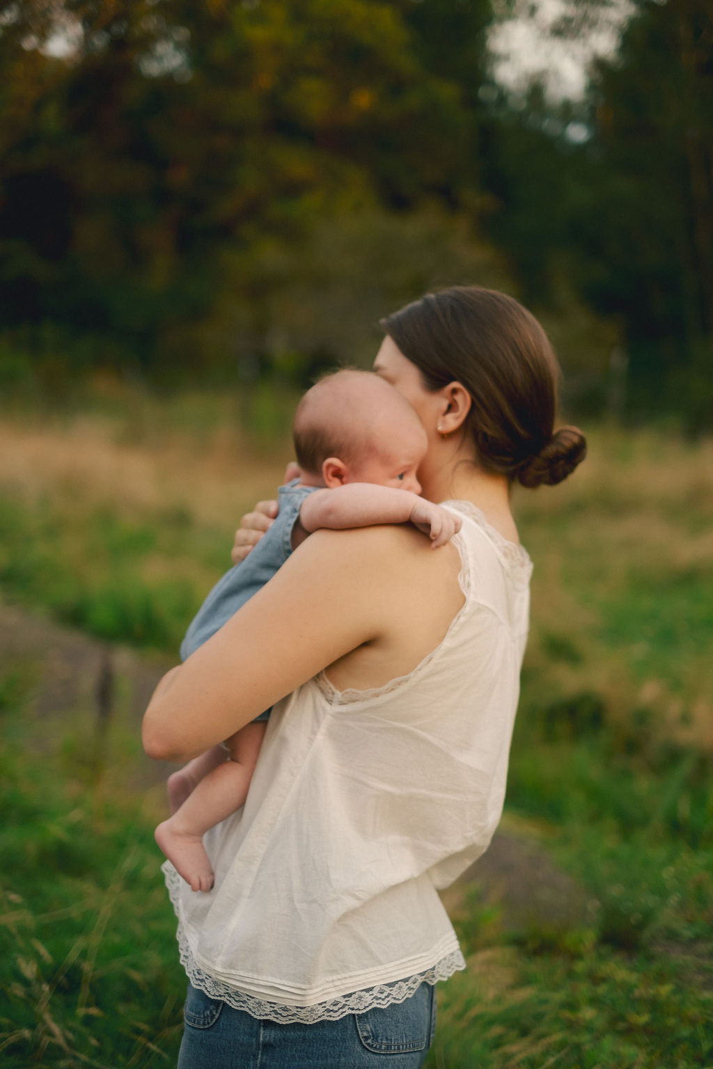 Woman holding a baby outdoors in a grassy area with trees in the background.