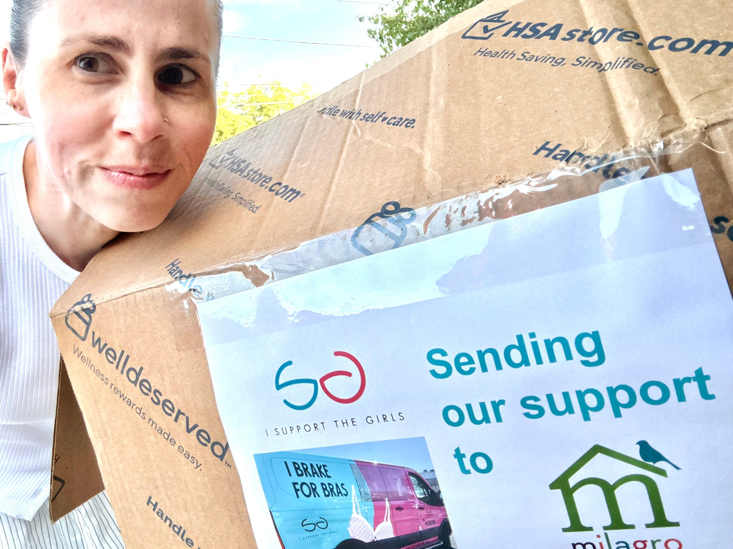 Woman holding a cardboard box with a label supporting a children's charity, outdoors with trees in background.
