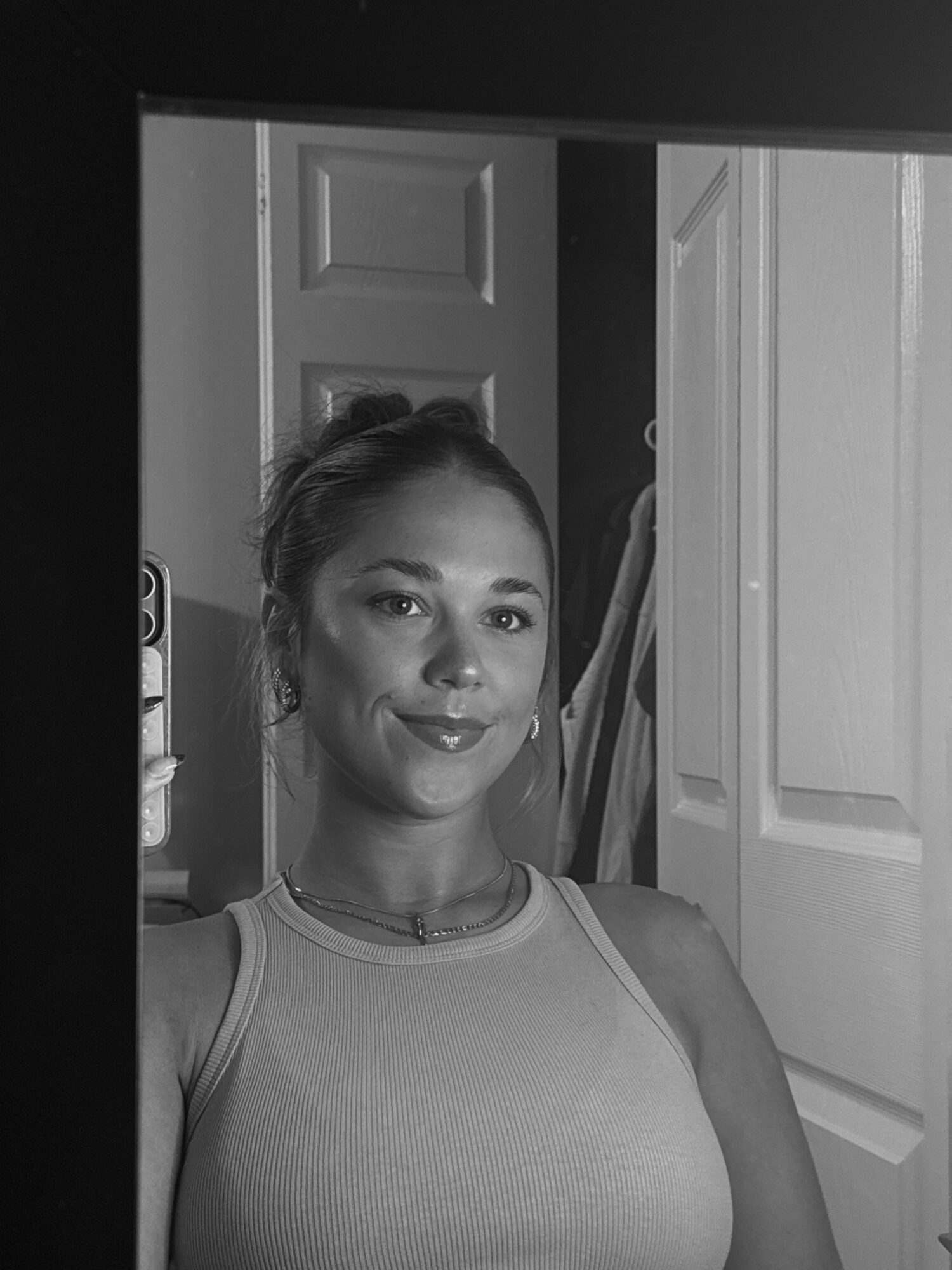 Woman with a slight smile taking a selfie in a room with closed doors, wearing a sleeveless top.
