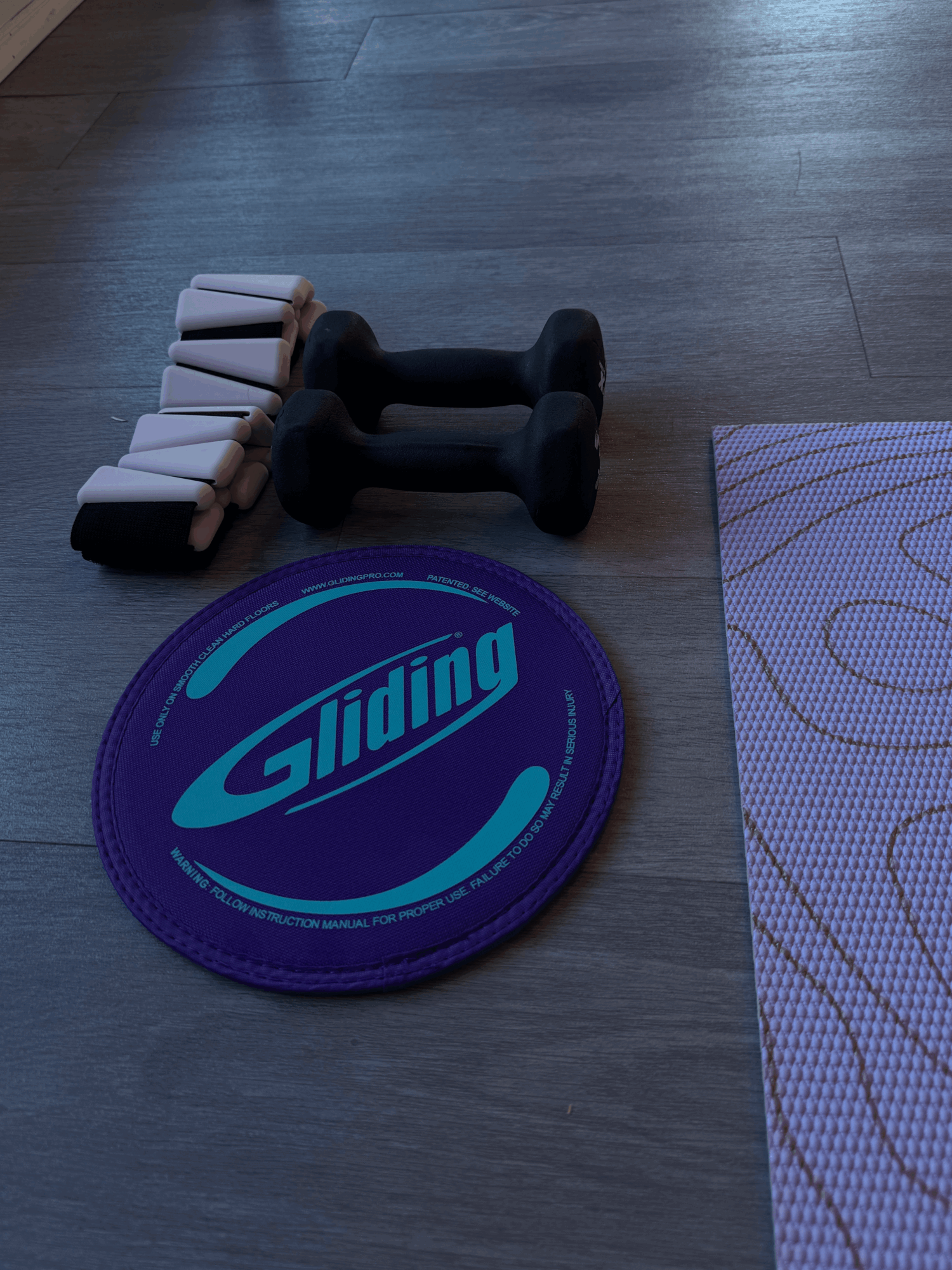 Dumbbells, a round purple Gilding mat, and a purple patterned mat on a wooden floor.