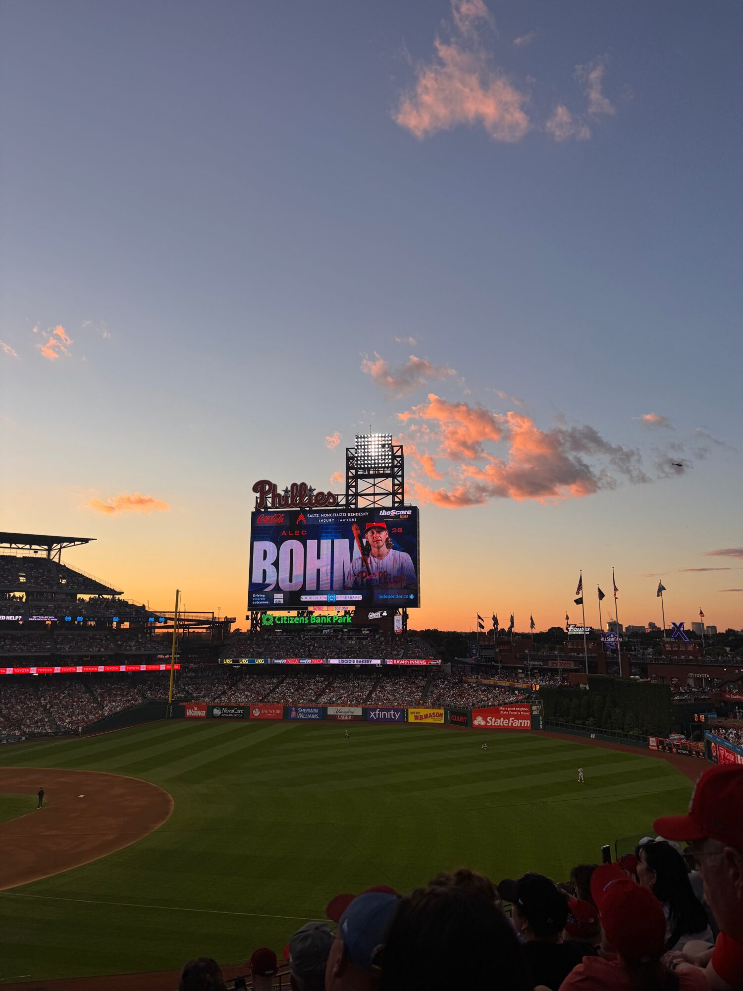 Baseball stadium with a large screen displaying a player, during sunset with a partly cloudy sky.