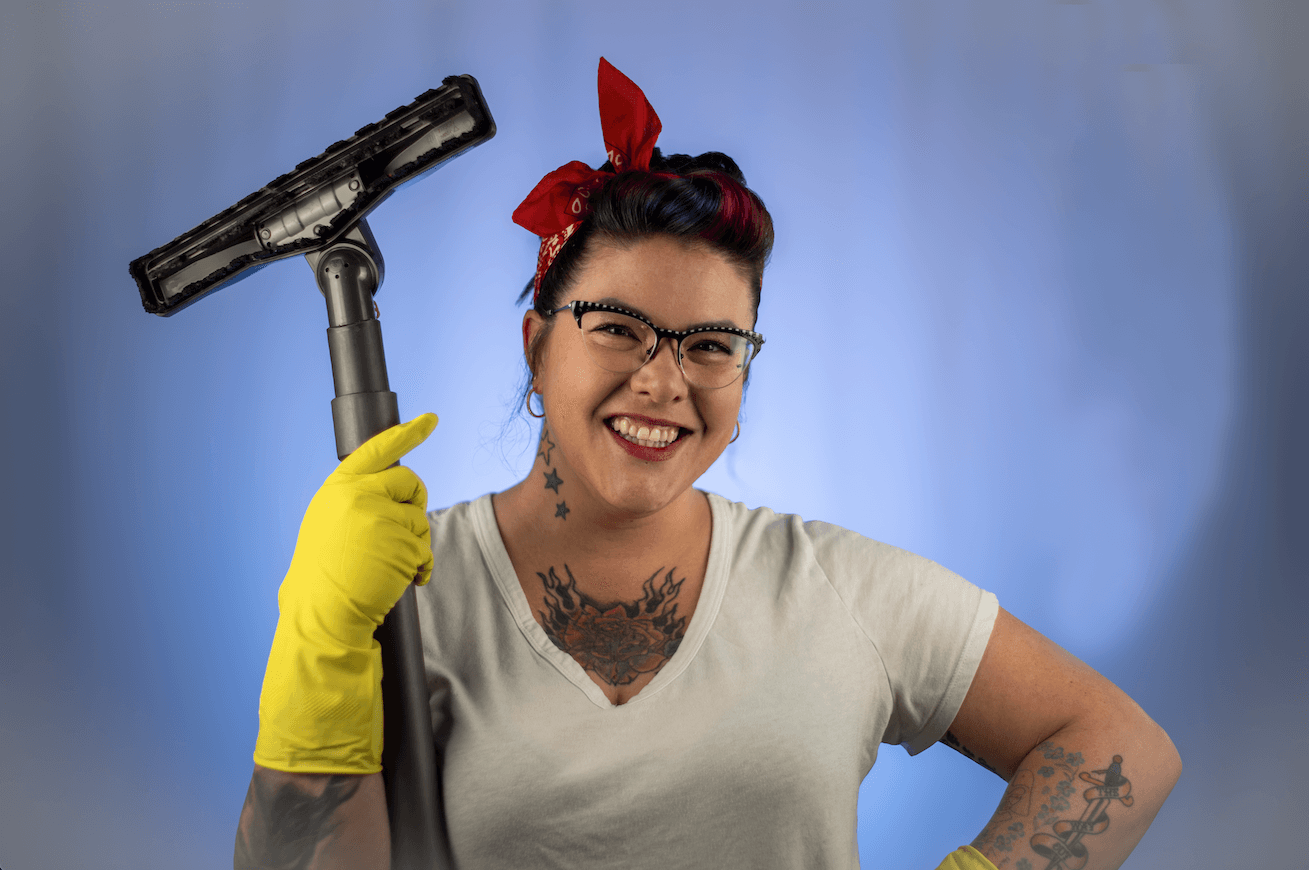 Woman with glasses, red headband, yellow glove, holding a power drill, smiling, against a blue background.