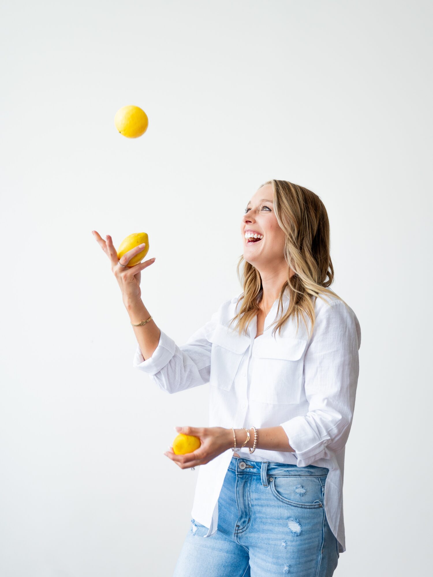 Woman smiling and juggling three yellow balls against a plain white background.