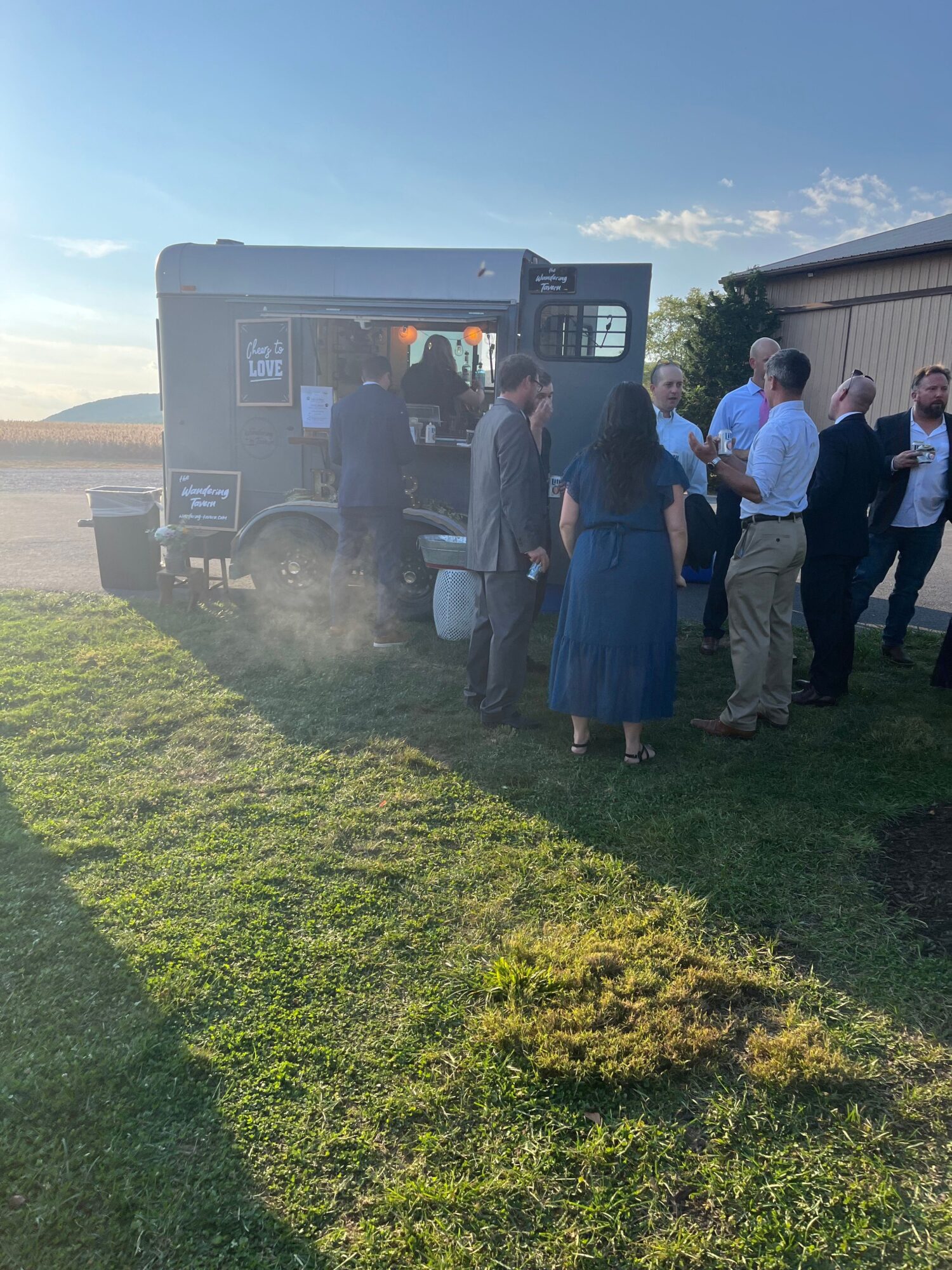 Group of people gathered around a food truck on a grassy area during daytime.