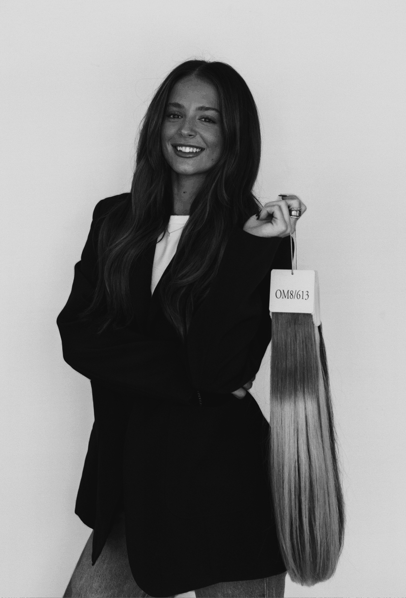 Woman with long hair holding a hair extension sample, smiling, in black and white.