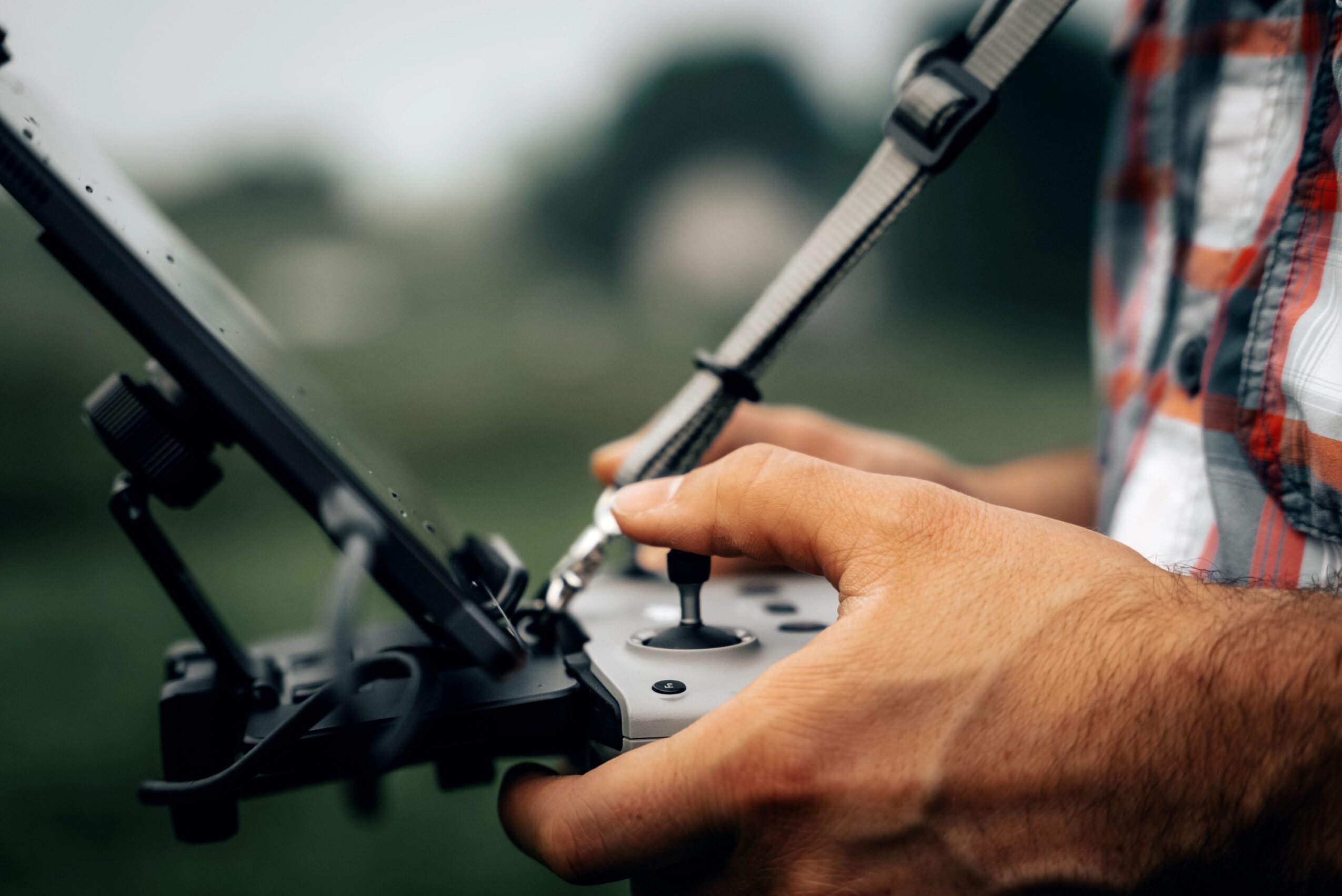 Person operating a drone controller outdoors, with a blurred background of trees and sky.
