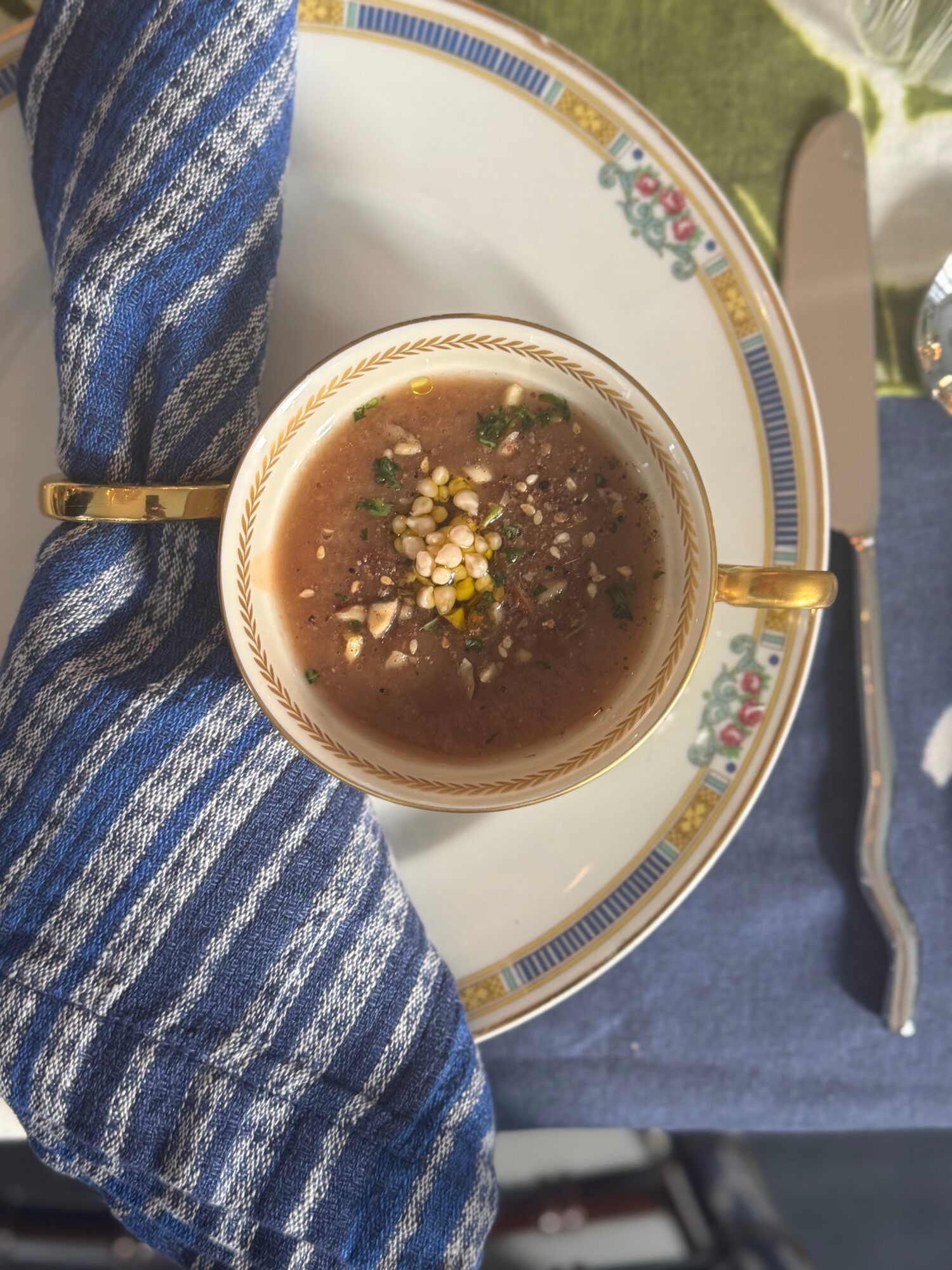 Cup of dark beverage with flower garnish on a decorative plate, blue cloth, knife, and outdoor setting