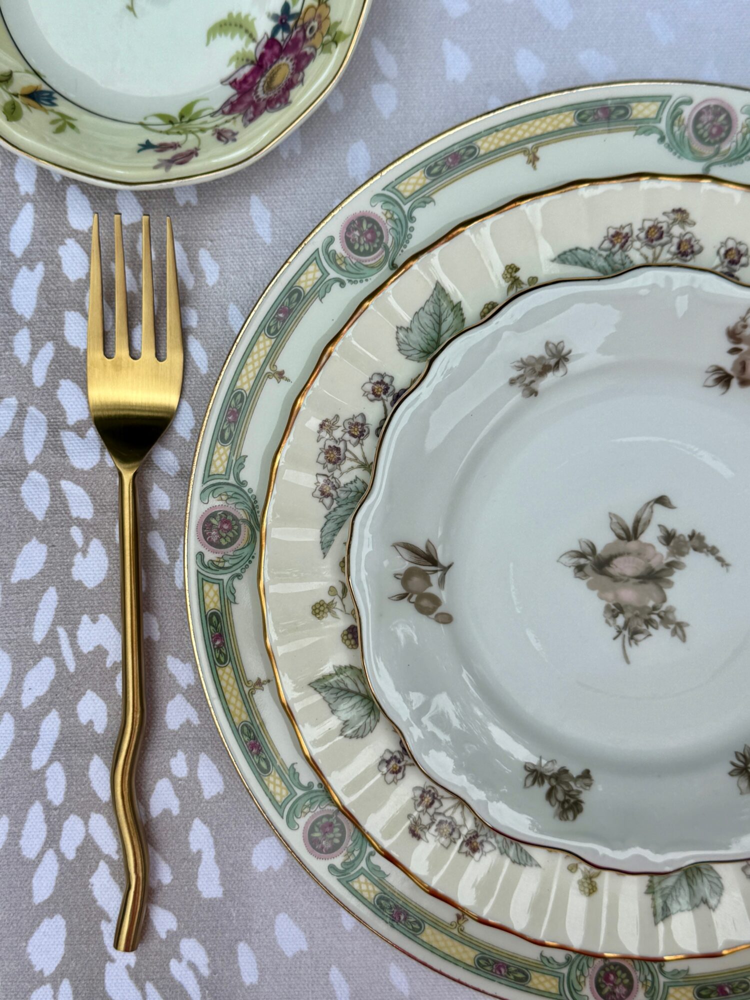 Elegant table setting with floral-patterned plates, a gold fork, and a tablecloth with white heart shapes.