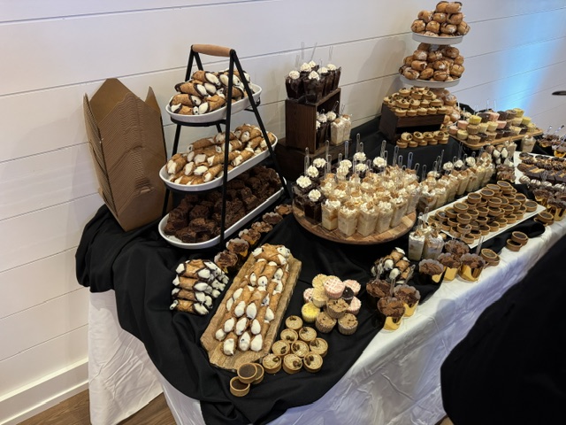 Dessert table with assorted sweets and treats on black and white tablecloths, with a white wall background.