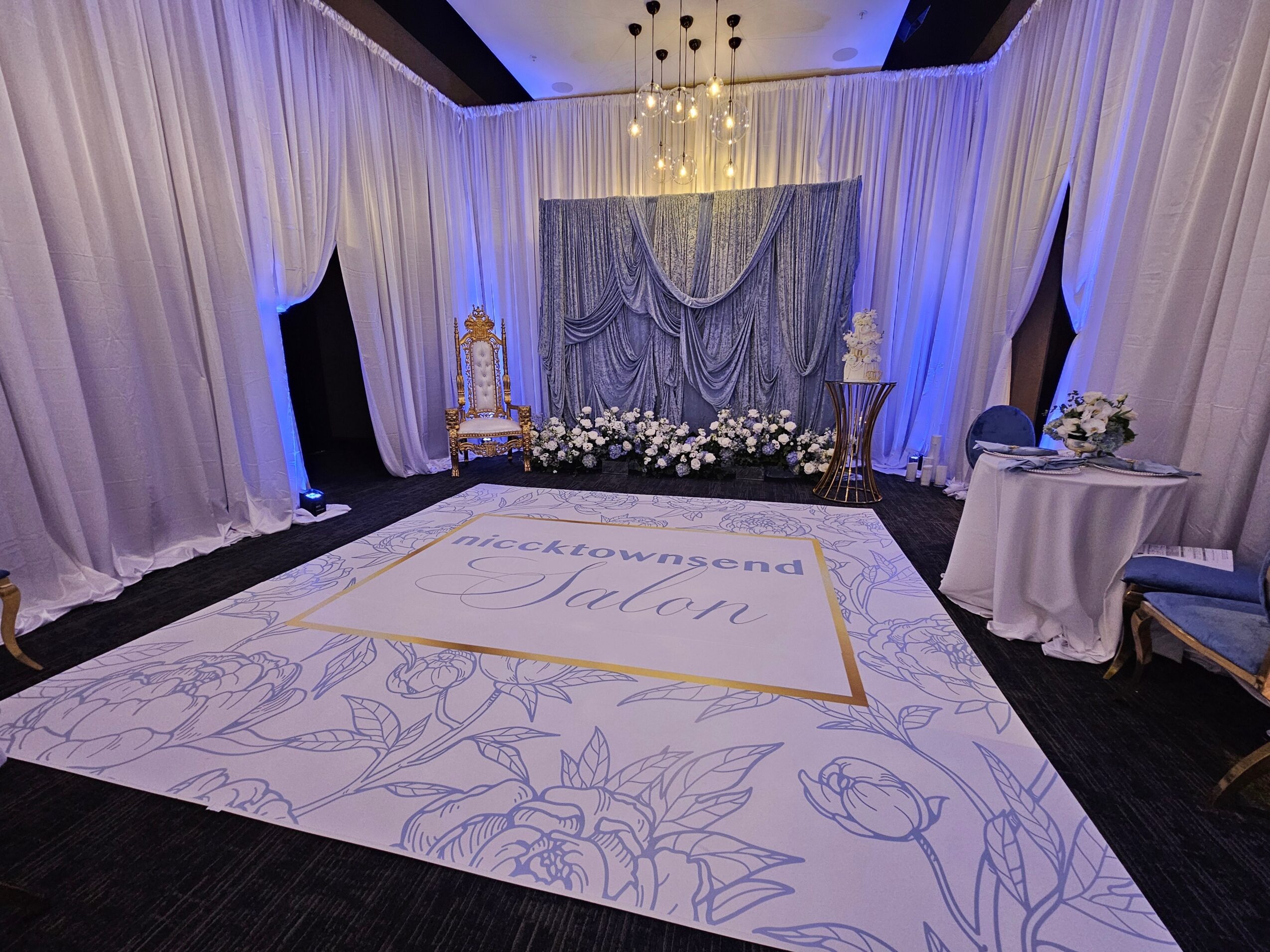 Elegant stage with draped curtains, floral arrangements, and a large decorated floor area for a wedding or event.