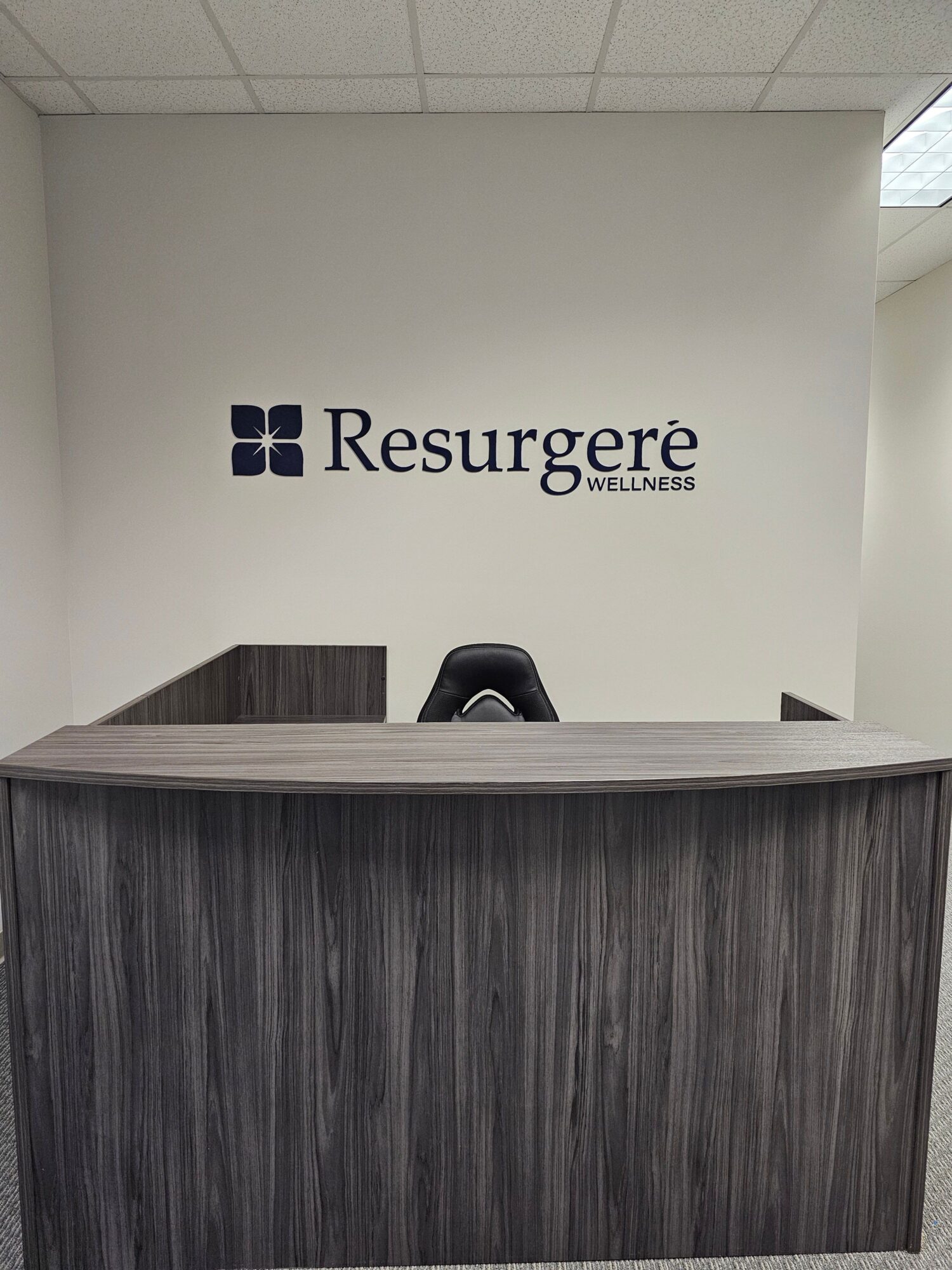Office reception area with a desk and a wall displaying the Resurge logo and text.