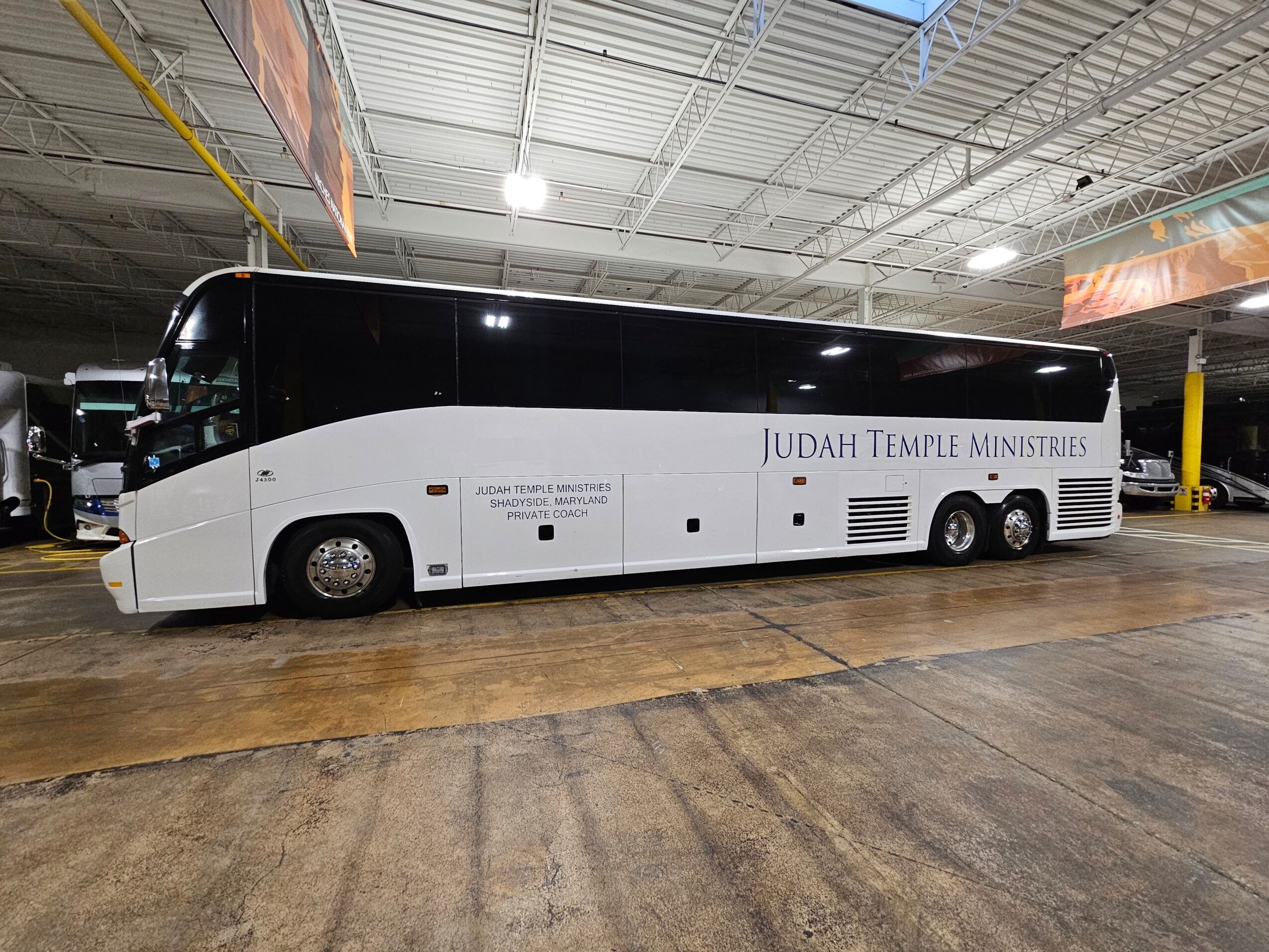 Large black and white bus parked inside a warehouse with a high ceiling and industrial lighting.