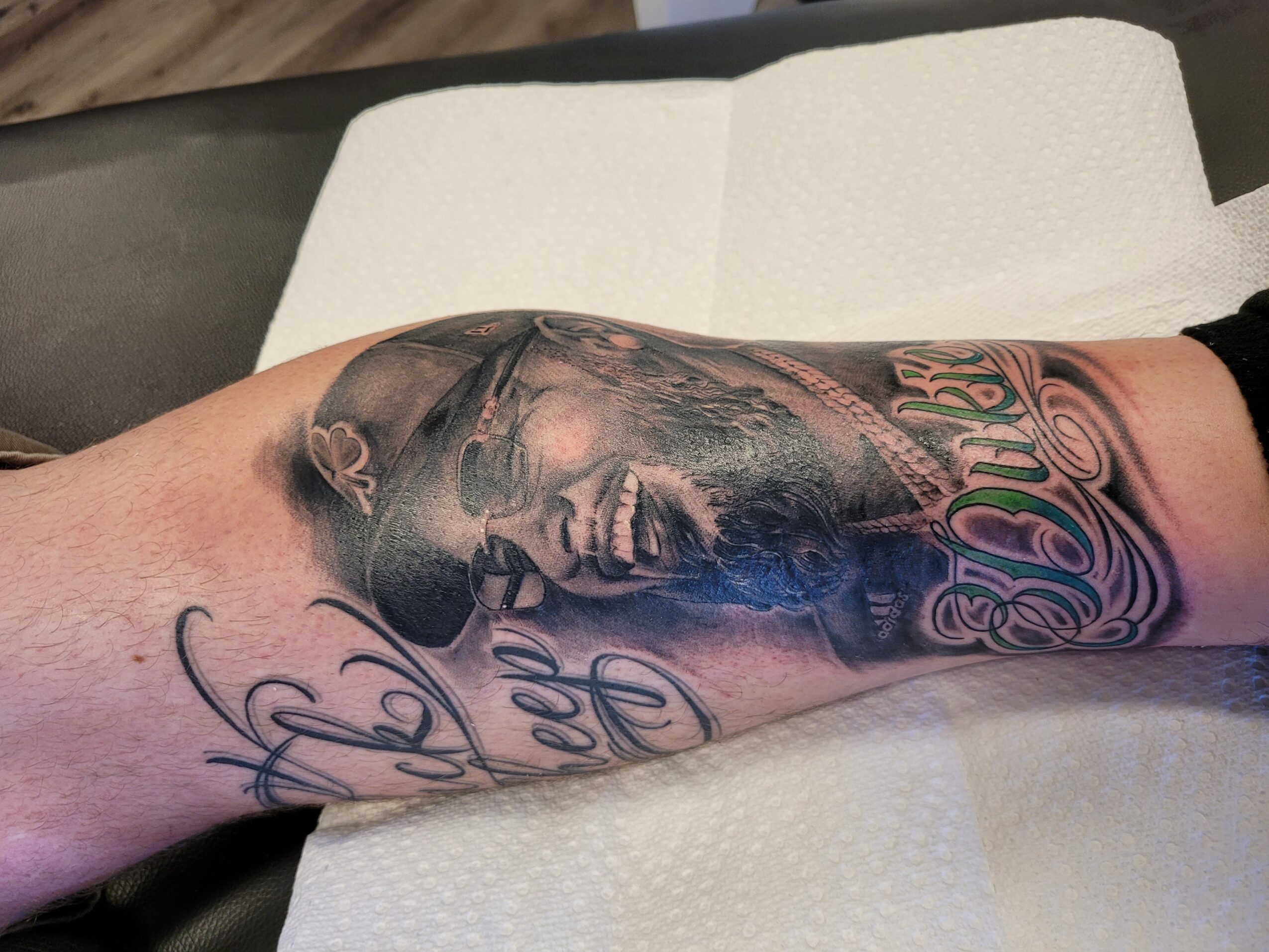 Tattoo of a smiling woman with long hair and text on forearm, in black and gray ink.