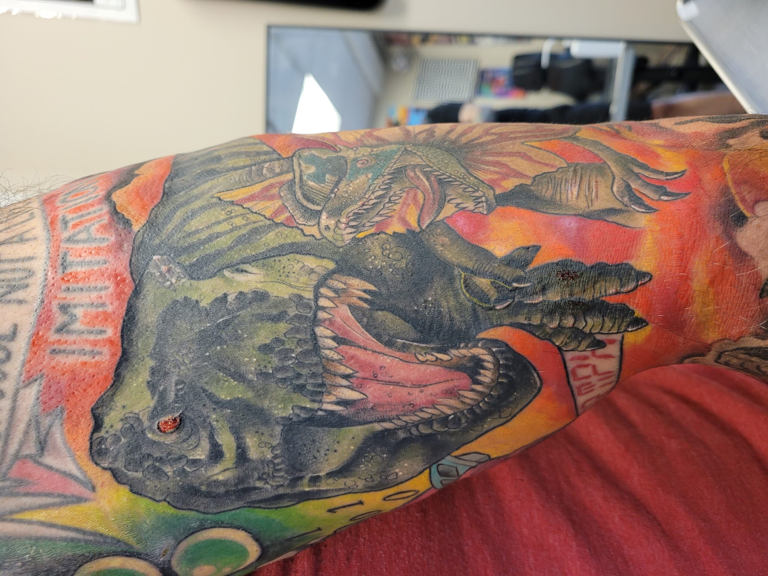 Tattoo of a dinosaur with an open mouth, detailed scales, and vibrant colors on a person's arm.