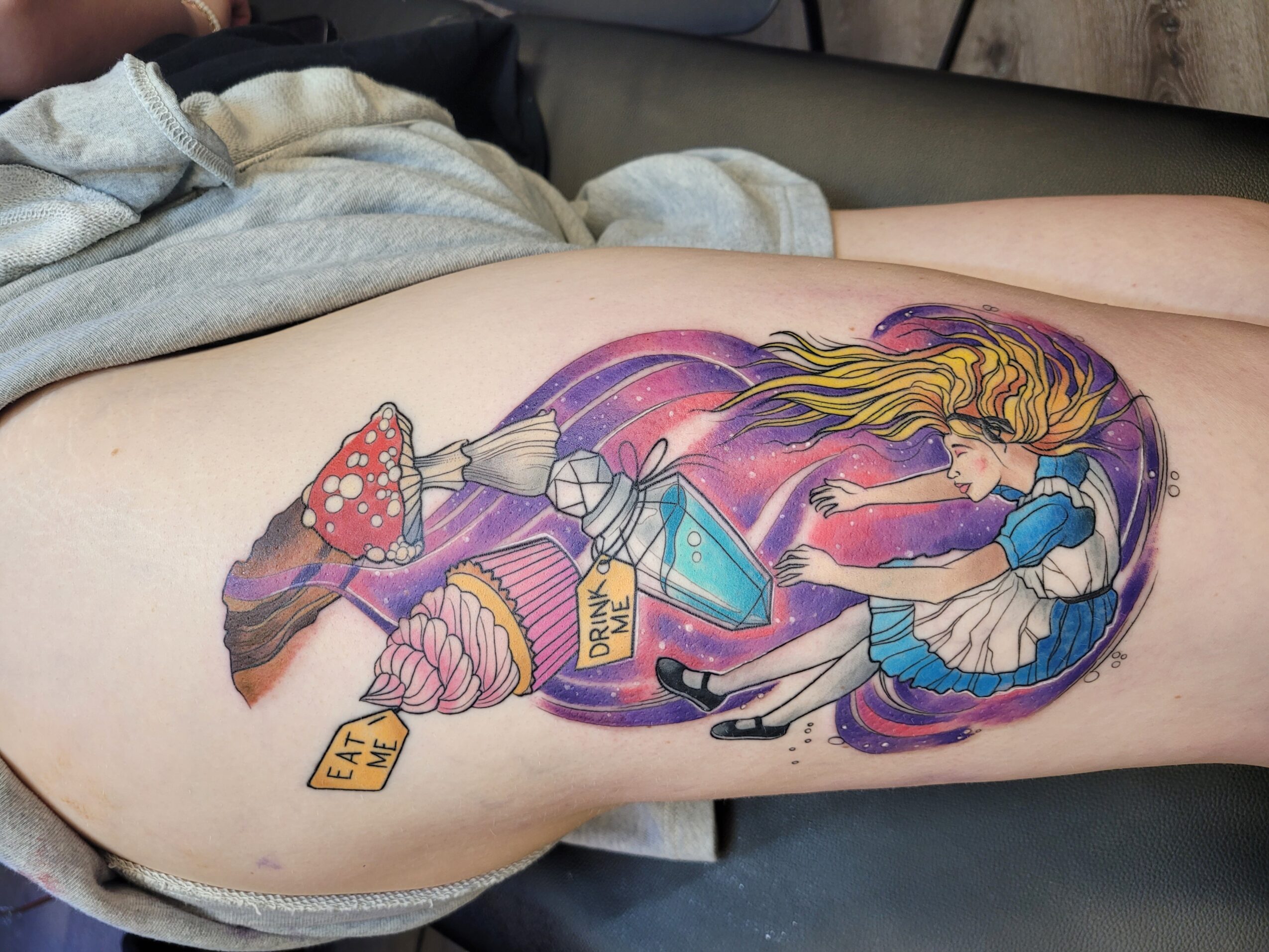 Colorful tattoo of a girl with long hair holding a blue diamond, surrounded by stars and a yellow sign, on thigh.