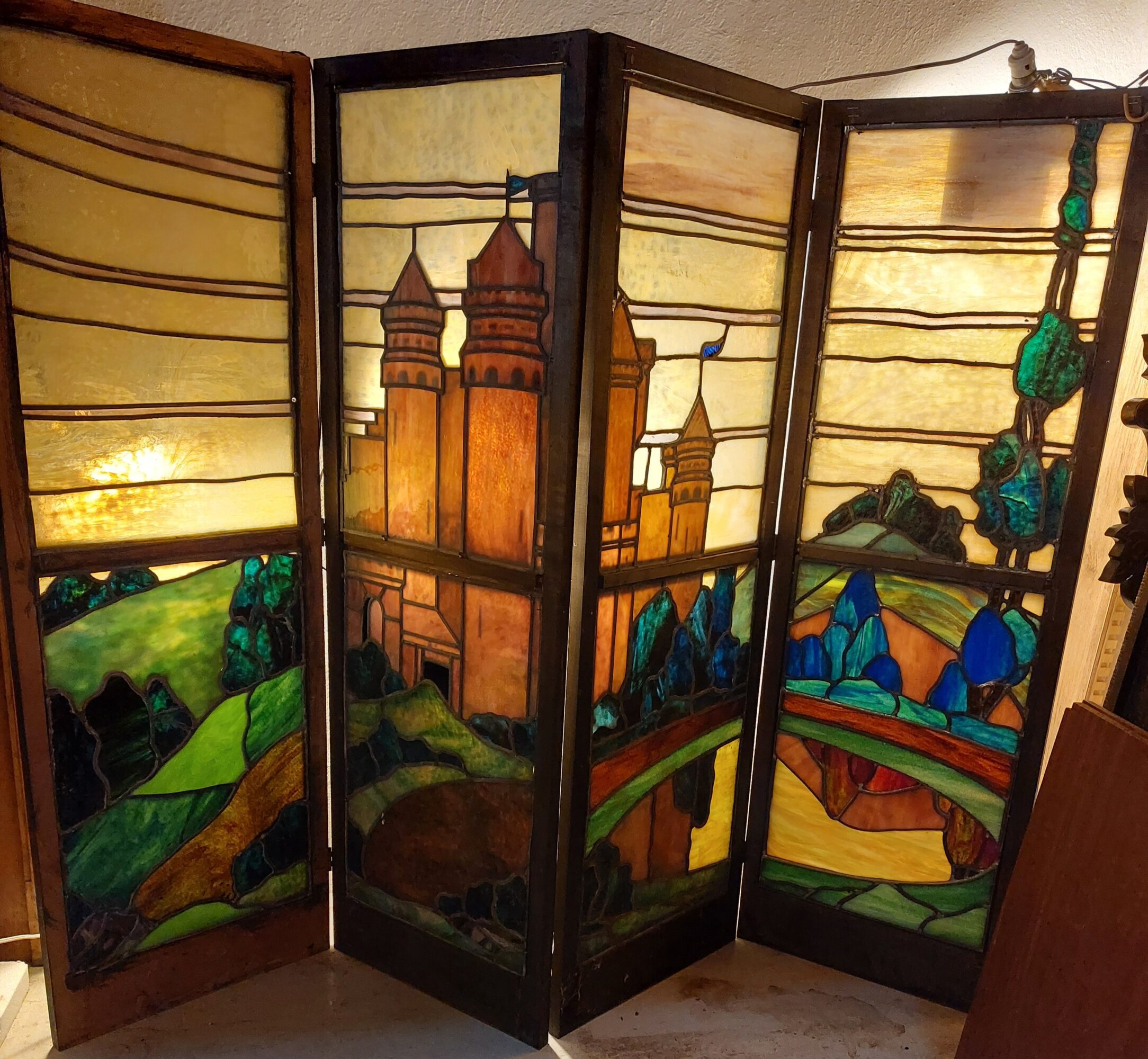 Four-panel stained glass room divider with a castle, trees, and landscape scenes, viewed from the side.