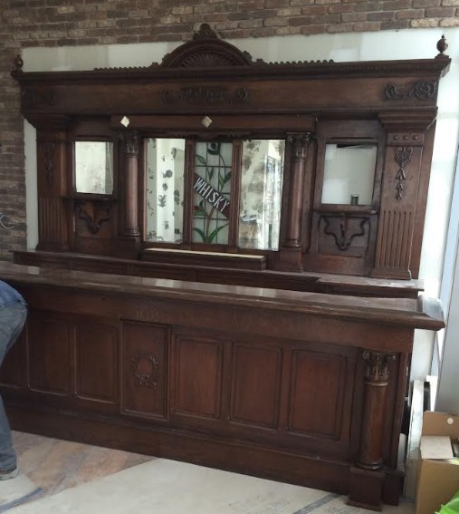 Large antique wooden cabinet with glass doors and intricate carvings, set against a brick wall, with a brick floor nearby.