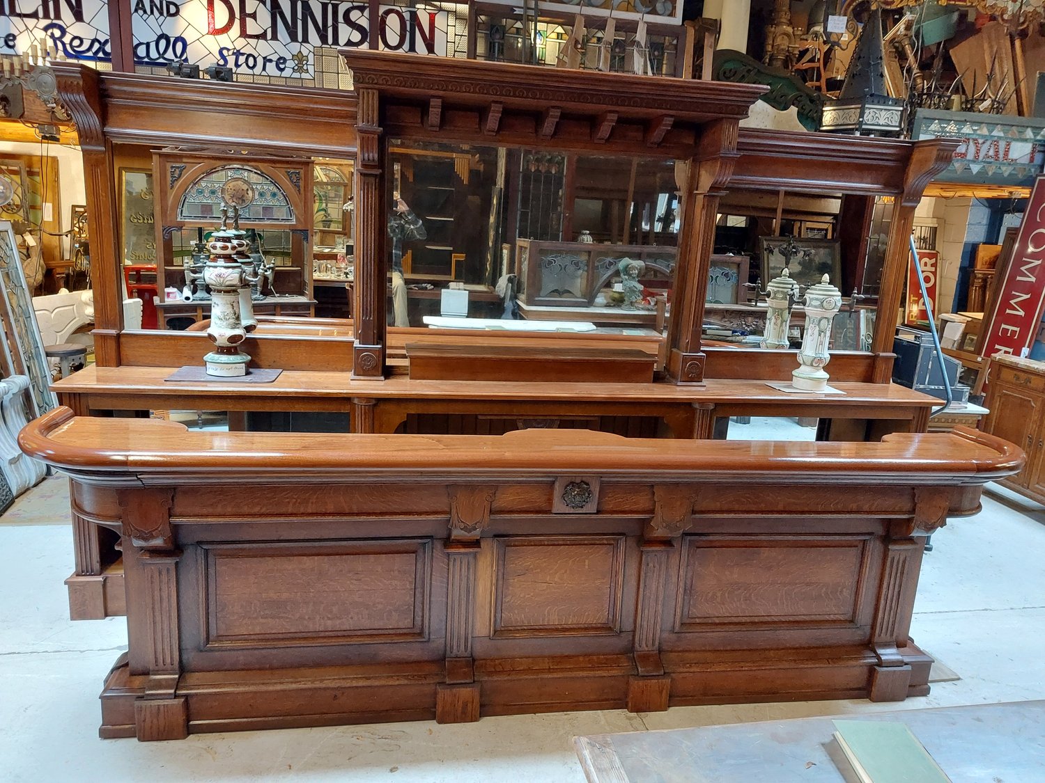 Wooden bar counter with a mirror and glass display shelves, in a store setting, with various items around.