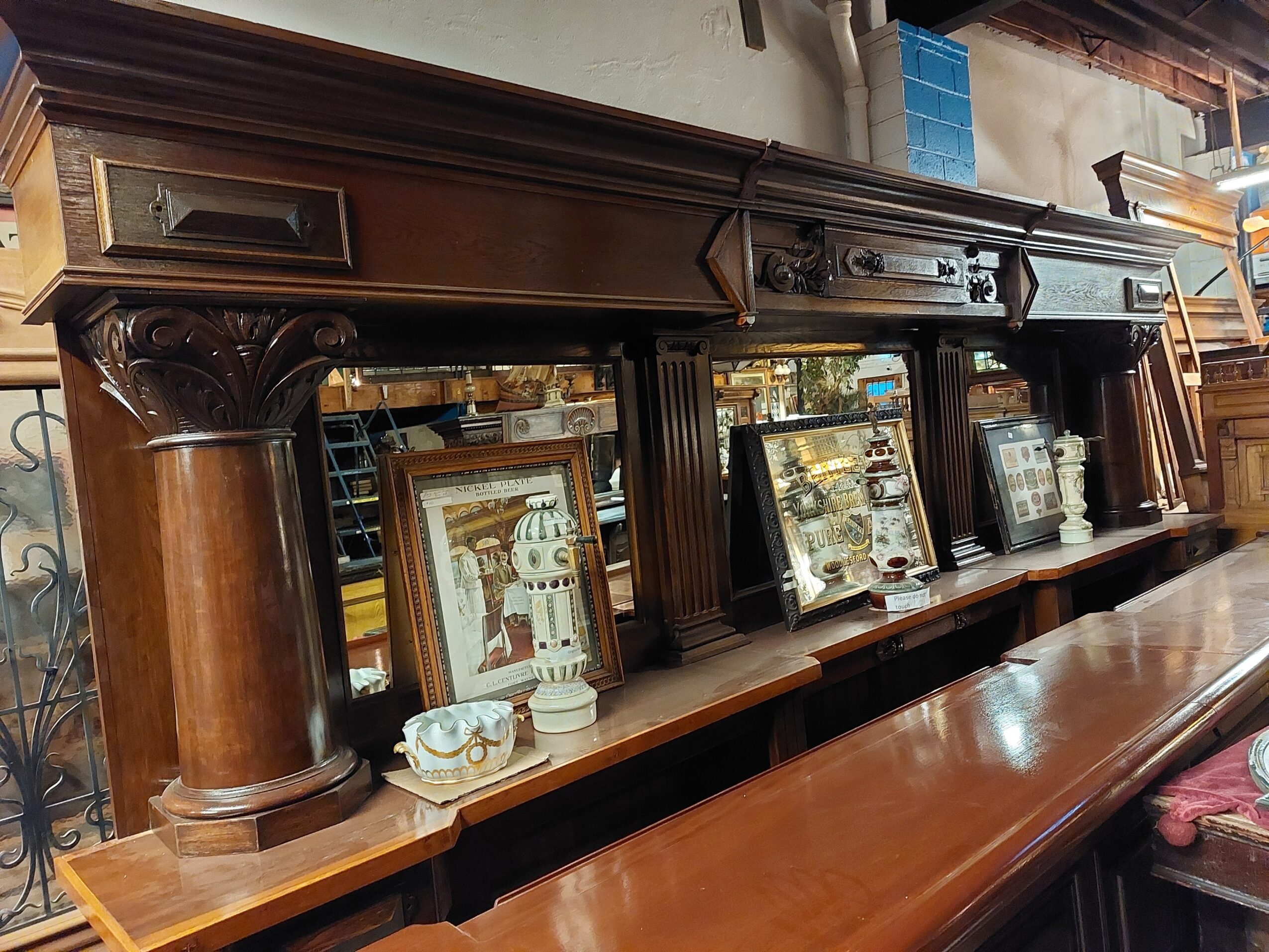 Long wooden antique sideboard with ornate columns and framed pictures on top, in a room with shelves and various items.