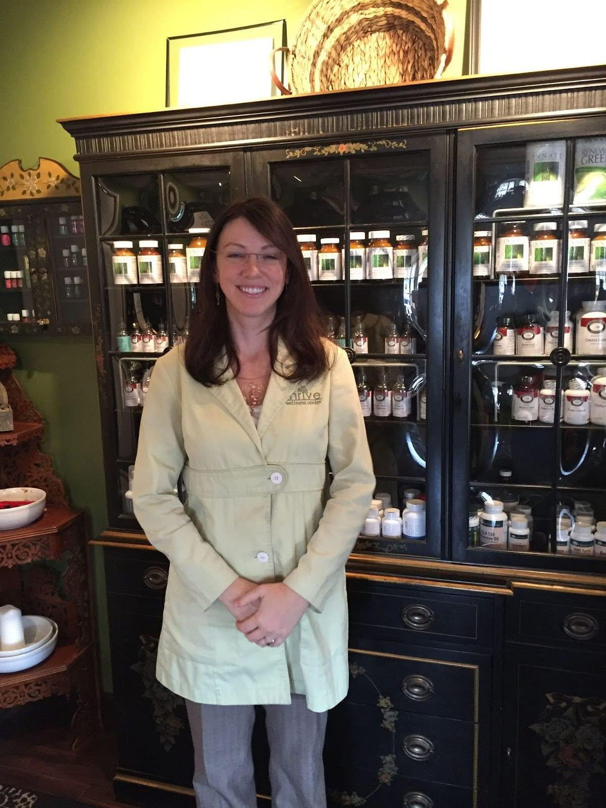 Woman standing in front of a black display cabinet filled with jars and dishes, smiling, in a room with green walls.
