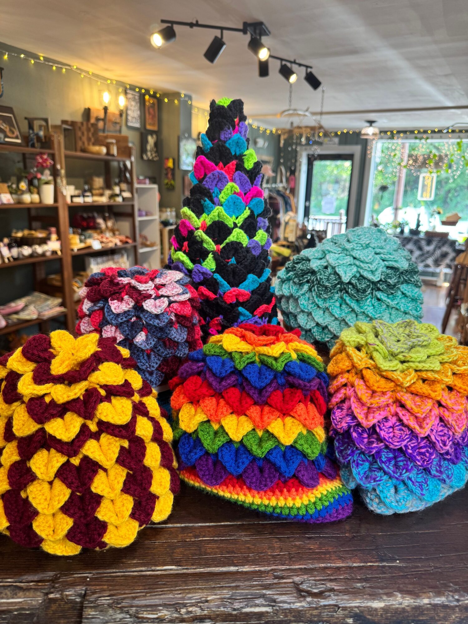 Colorful knitted hats arranged on a wooden surface inside a shop with shelves and lights in the background.