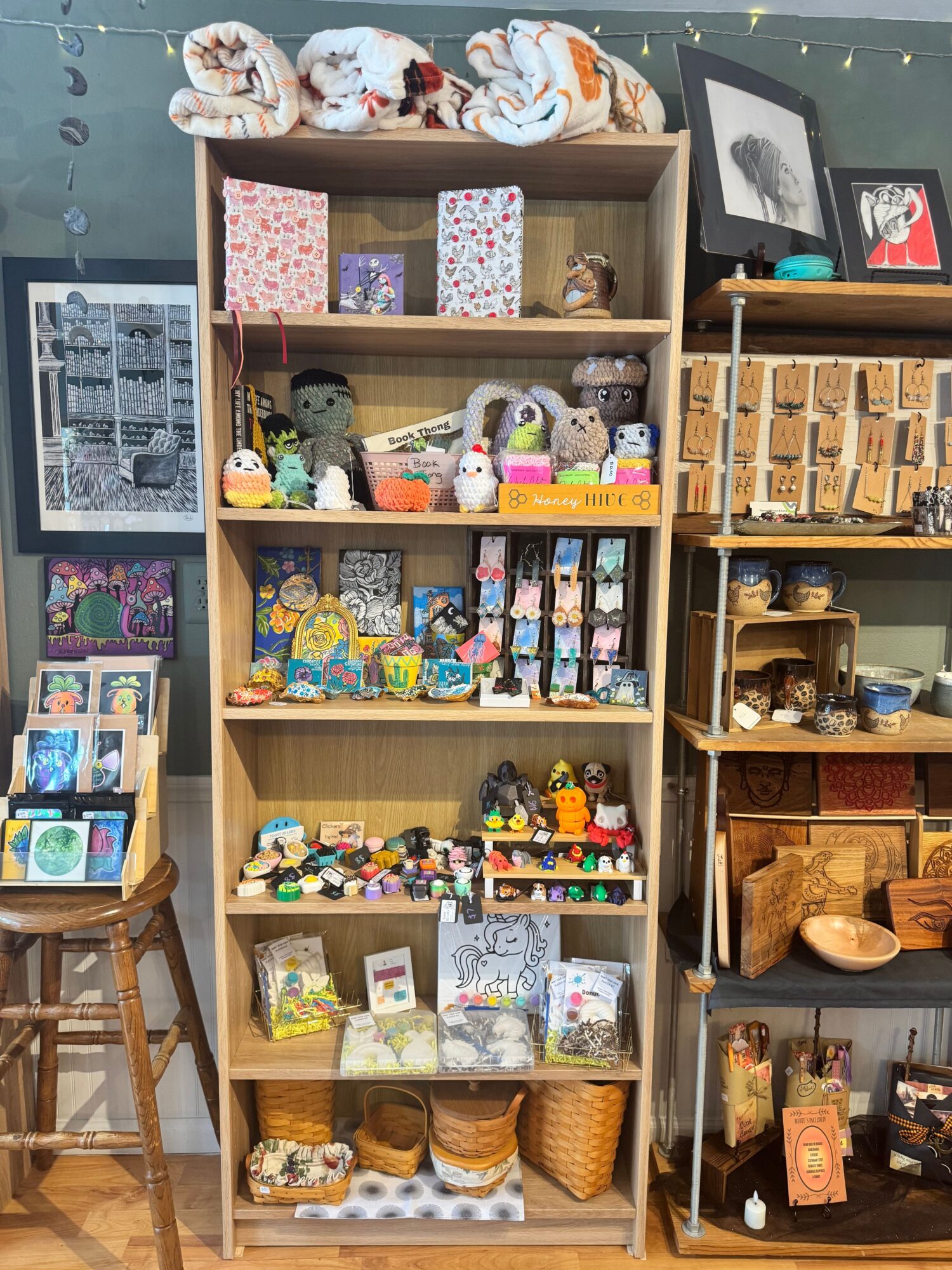 Display of small decorative items, figurines, and crafts arranged in wooden shelves and boxes, with some framed pictures and textiles.