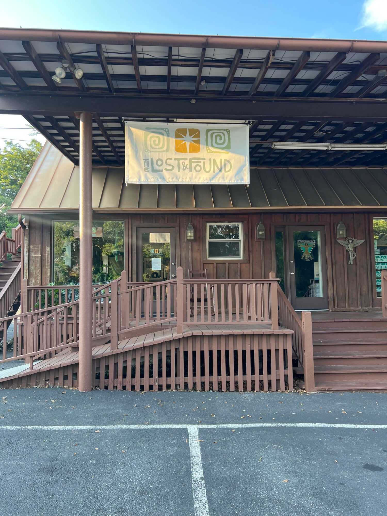 Wooden building with a porch, stairs, and a sign that reads 'Visit Us' in a parking lot.