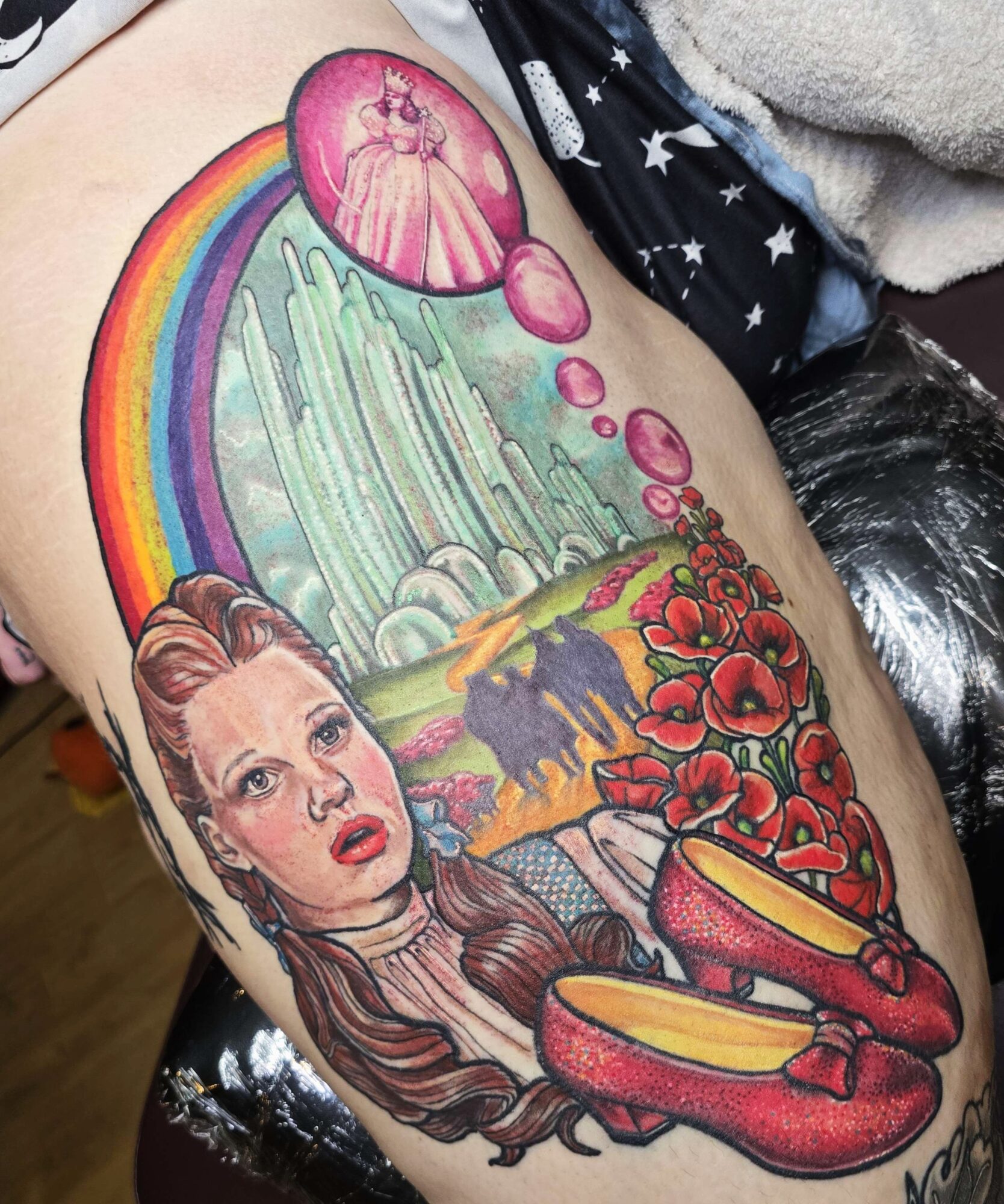 Tattoo of a woman with long hair, a rainbow, a waterfall, red flowers, and a pink shoe with yellow inside.