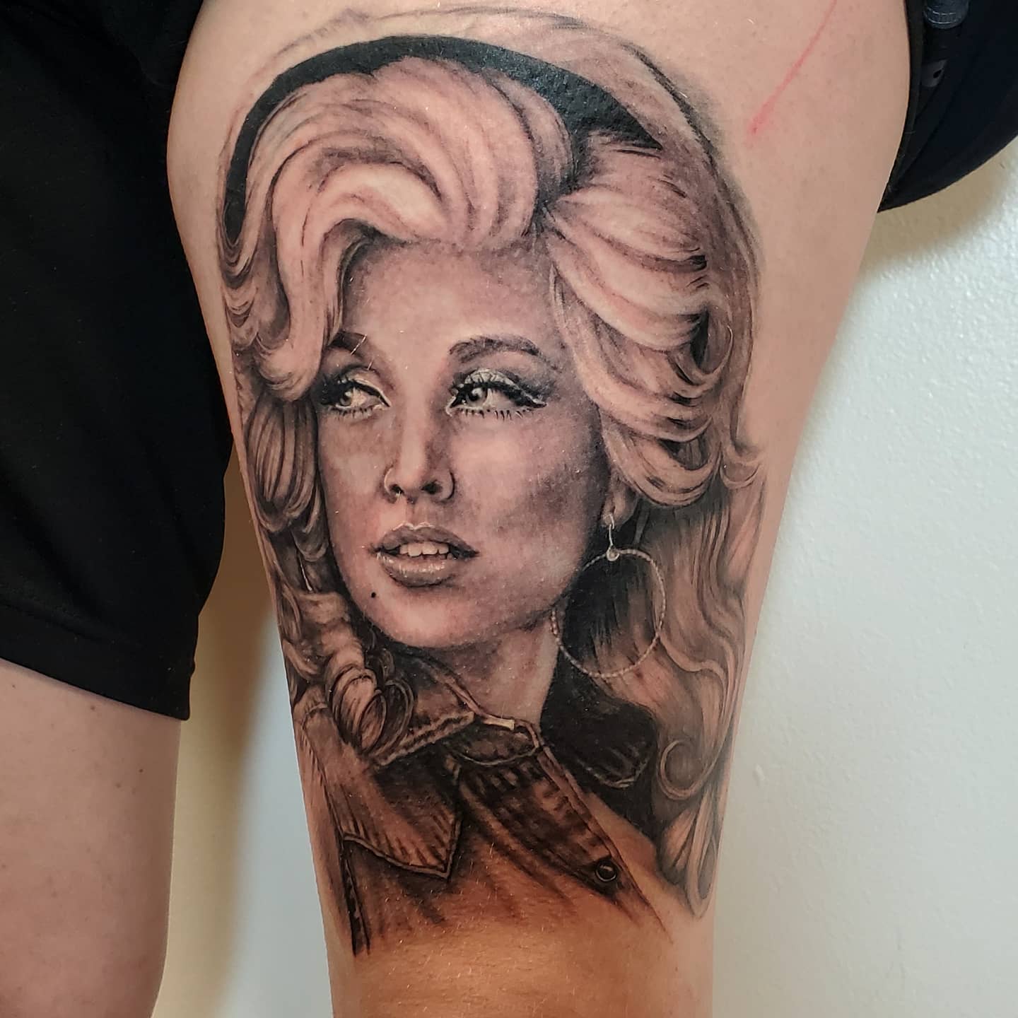 Realistic black and gray portrait of a woman with styled hair, wearing a jacket and hoop earrings, on upper arm.