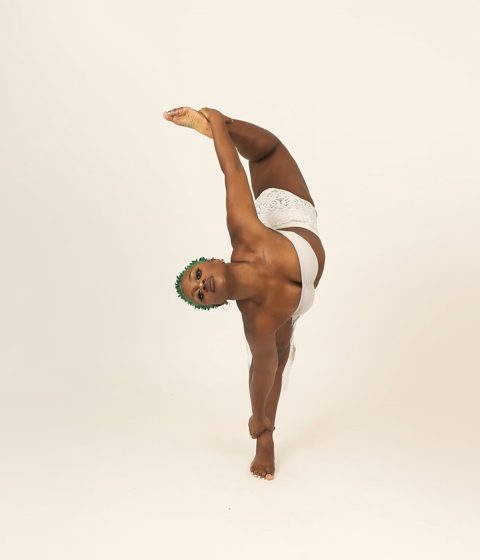 Person performing a standing split yoga pose, balancing on one leg with the other leg extended upward, against a plain background.