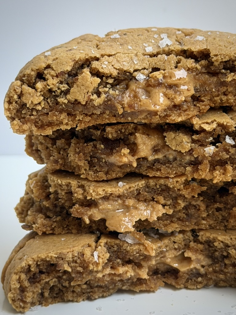 Stack of four chocolate chip cookies with visible melted chocolate, on a plain background.