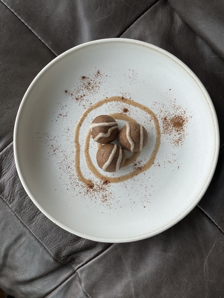 A white plate with a dessert topped with chocolate, surrounded by cocoa powder and caramel sauce, on a dark surface.