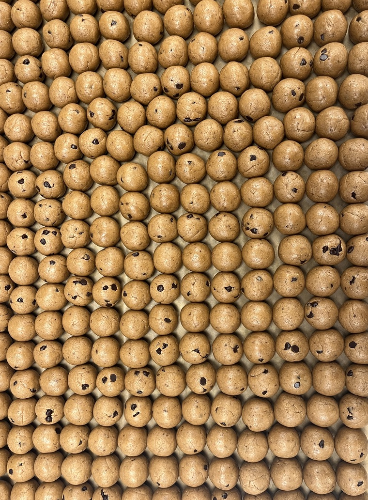 Close-up of numerous round, light brown wooden beads with small holes, arranged in a dense pattern.