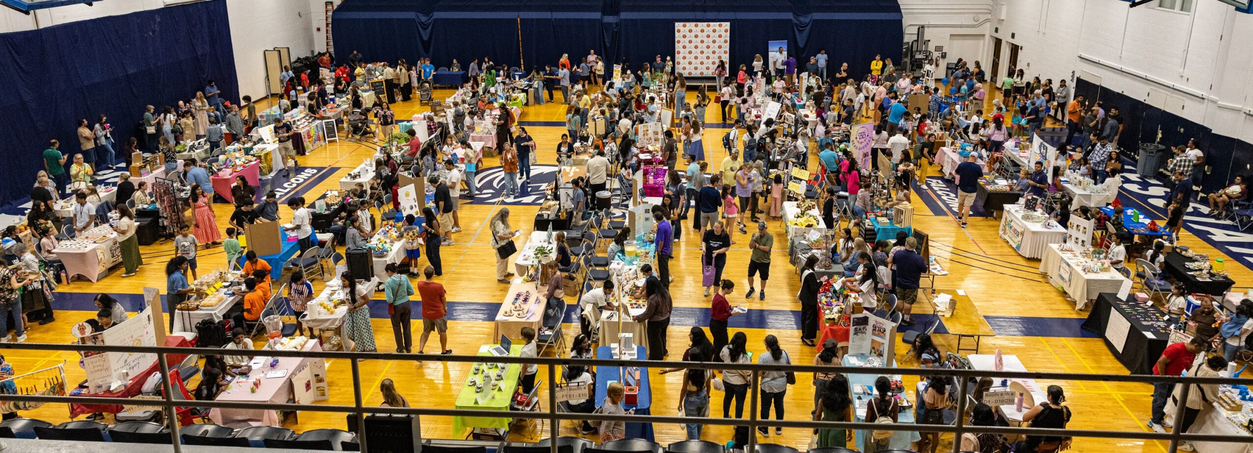 Large indoor event with many people, tables, and displays in a gymnasium or hall.