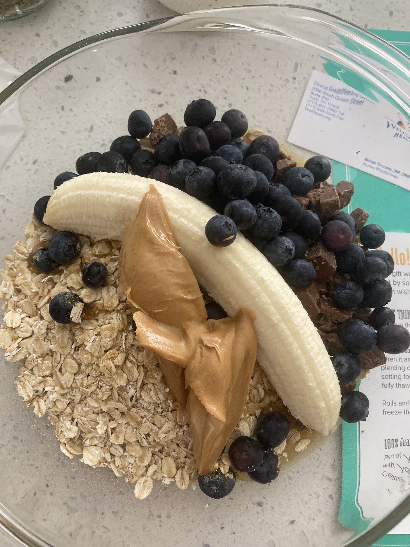 Oatmeal with banana, blueberries, and peanut butter in a glass bowl on a light surface.