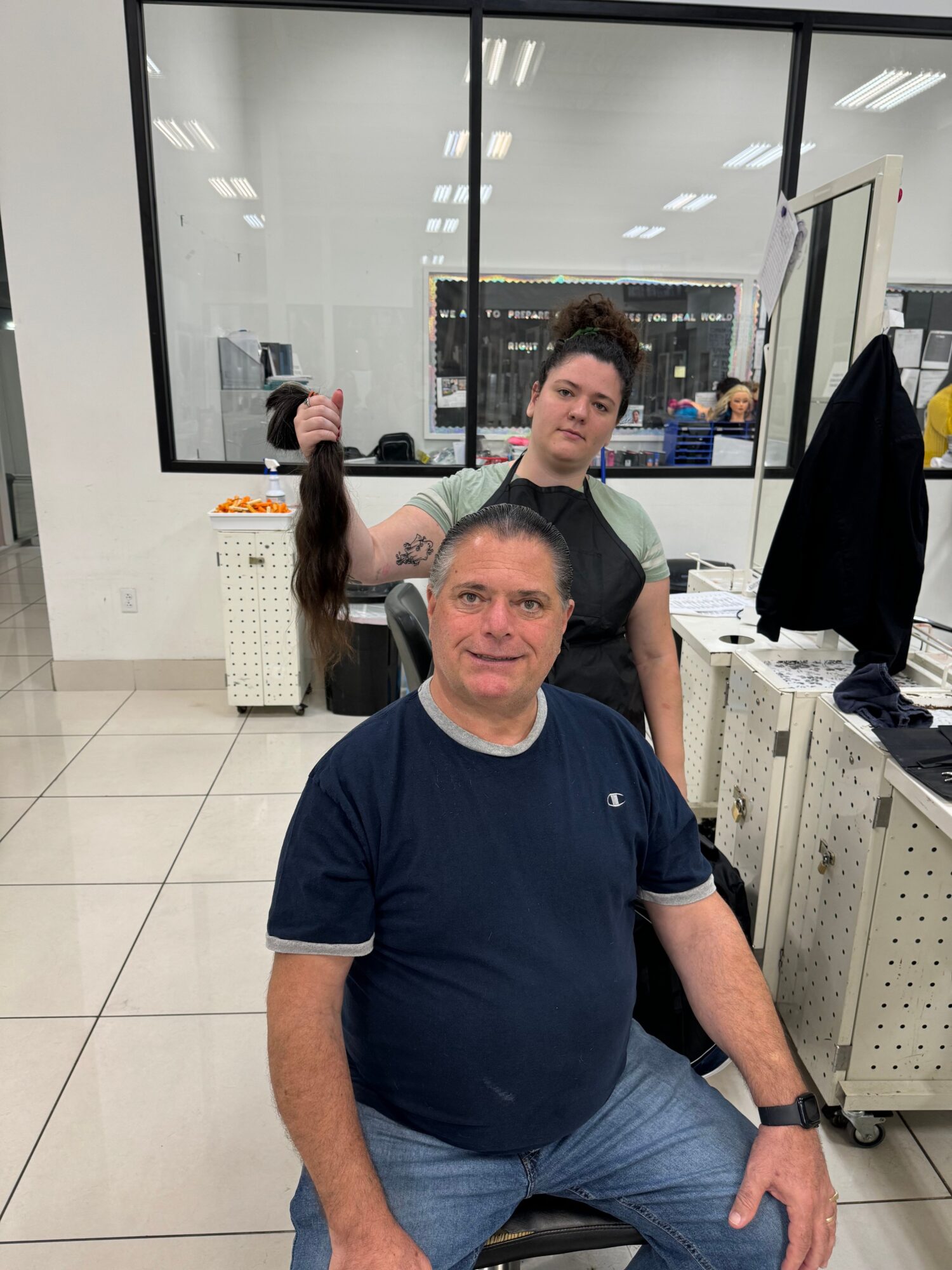 Two men in a store, one sitting and one standing, with shelves and a glass window behind them.