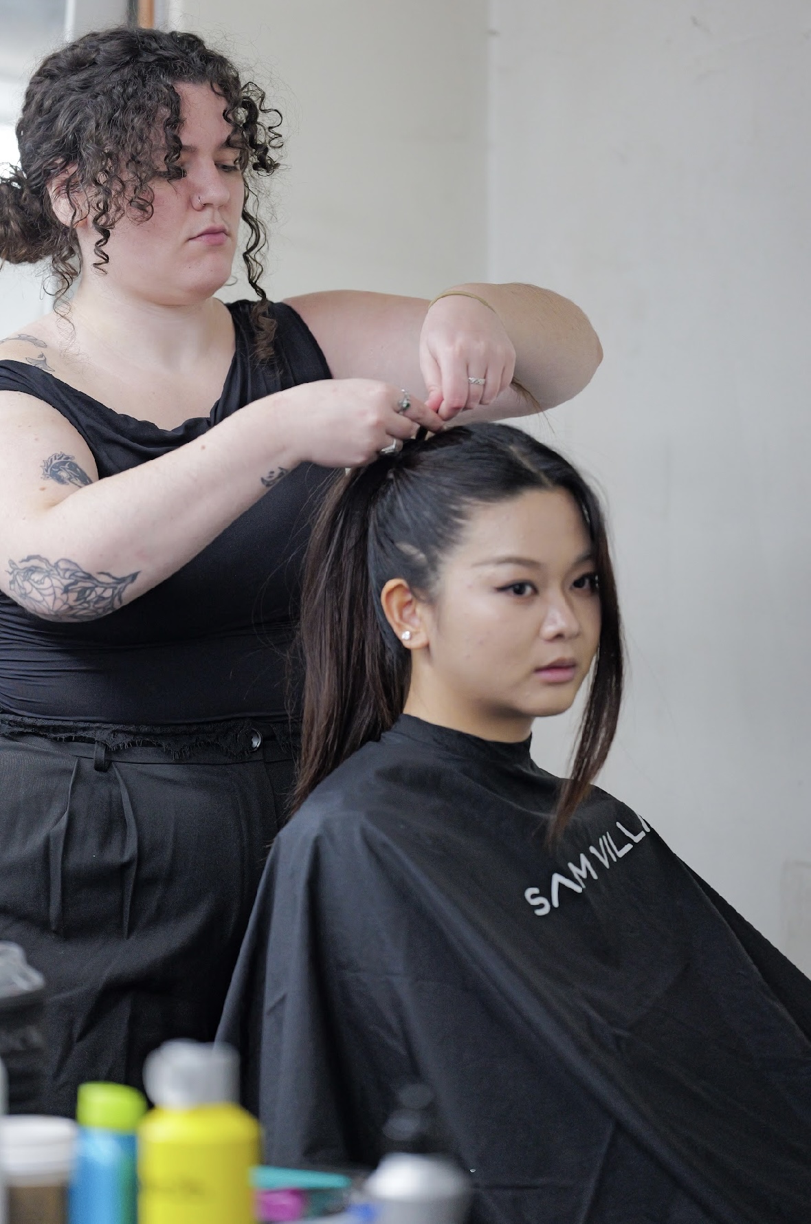 Hairdresser styles a woman's hair in a salon, with hair products visible in the foreground.