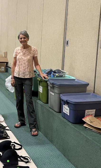 Woman standing next to storage bins and boxes in a room with beige walls and green carpet.