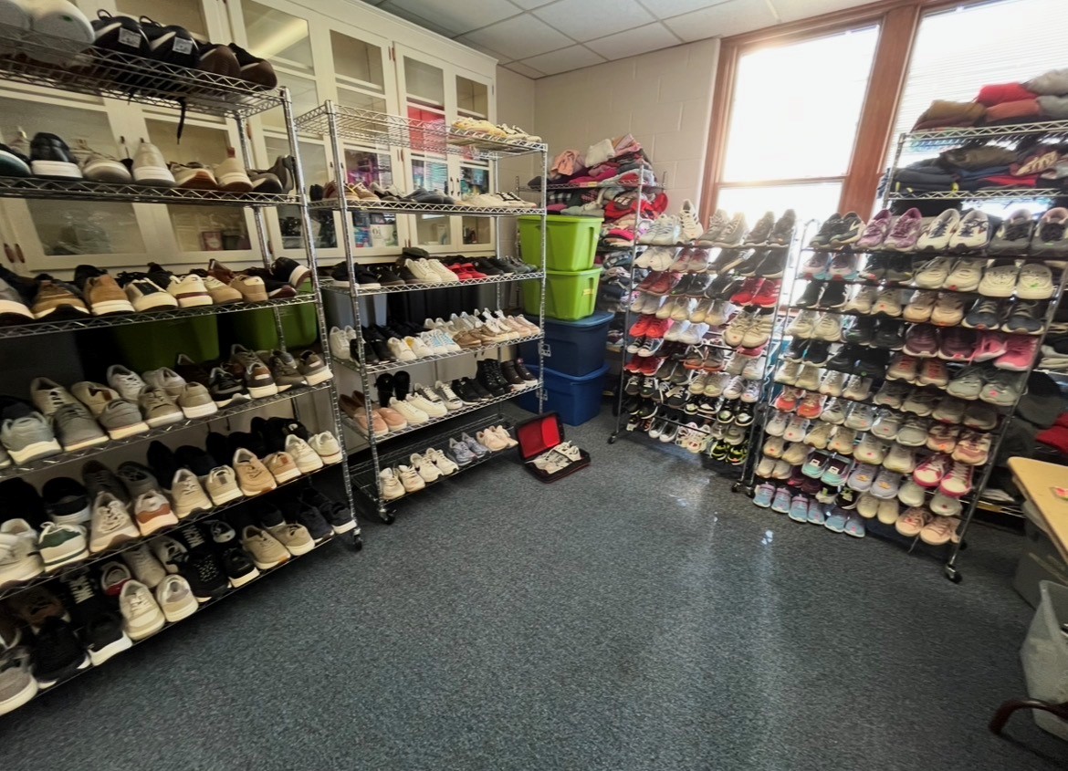 Room with shelves of shoes and storage bins, sunlight from windows, blue carpeted floor.