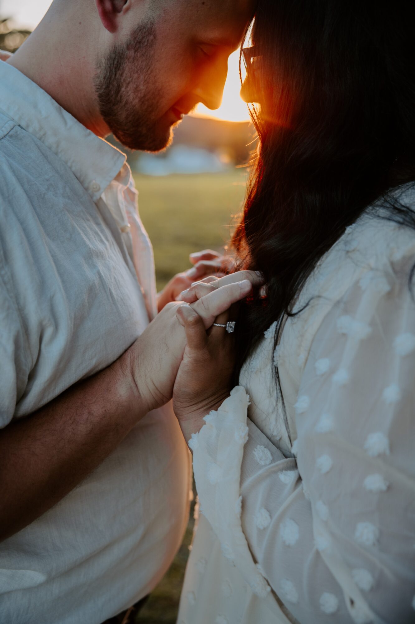 Close-up of a couple touching foreheads and holding hands outdoors during sunset.