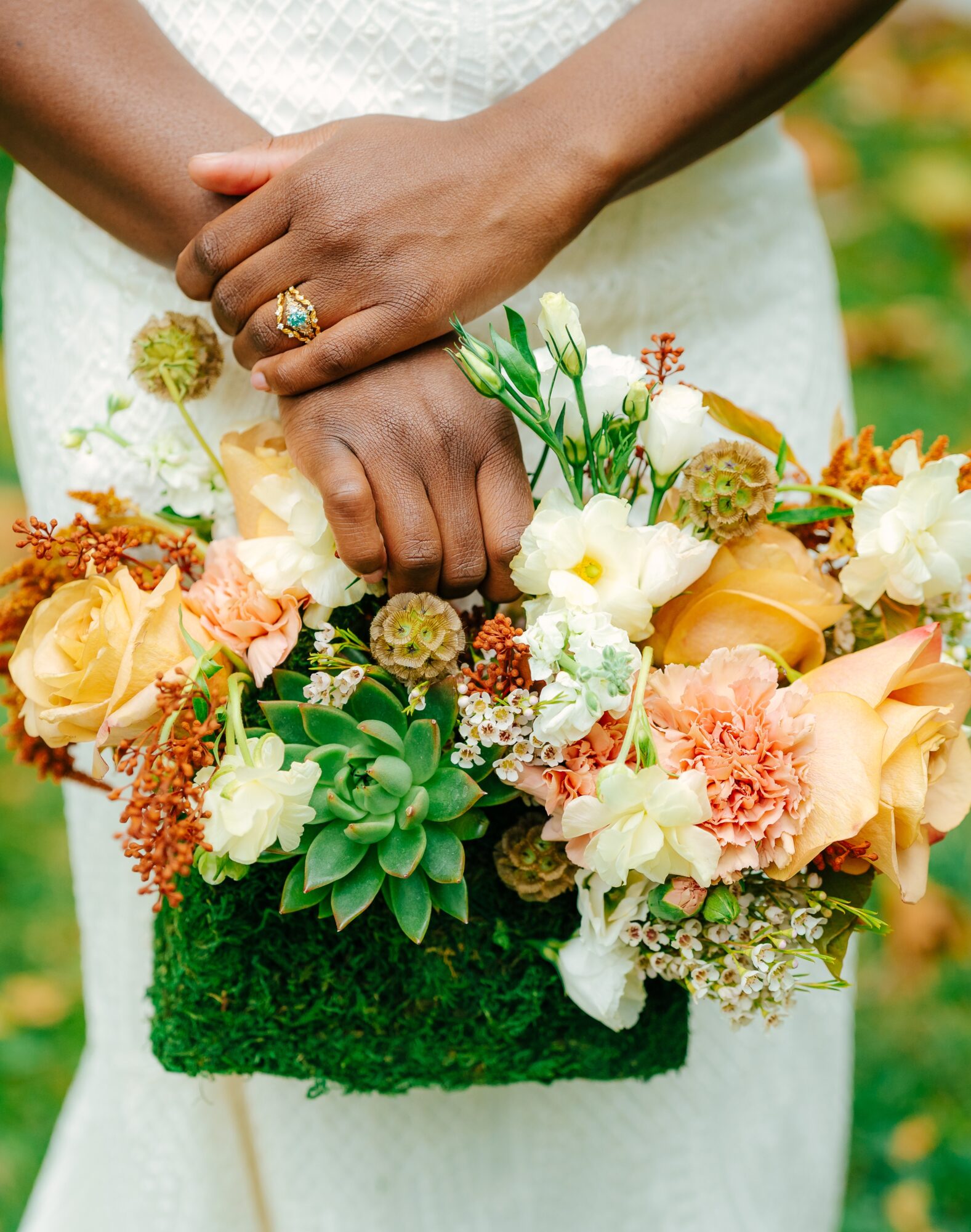 Person holding a bouquet of flowers with both hands, wearing a ring, in a garden setting.