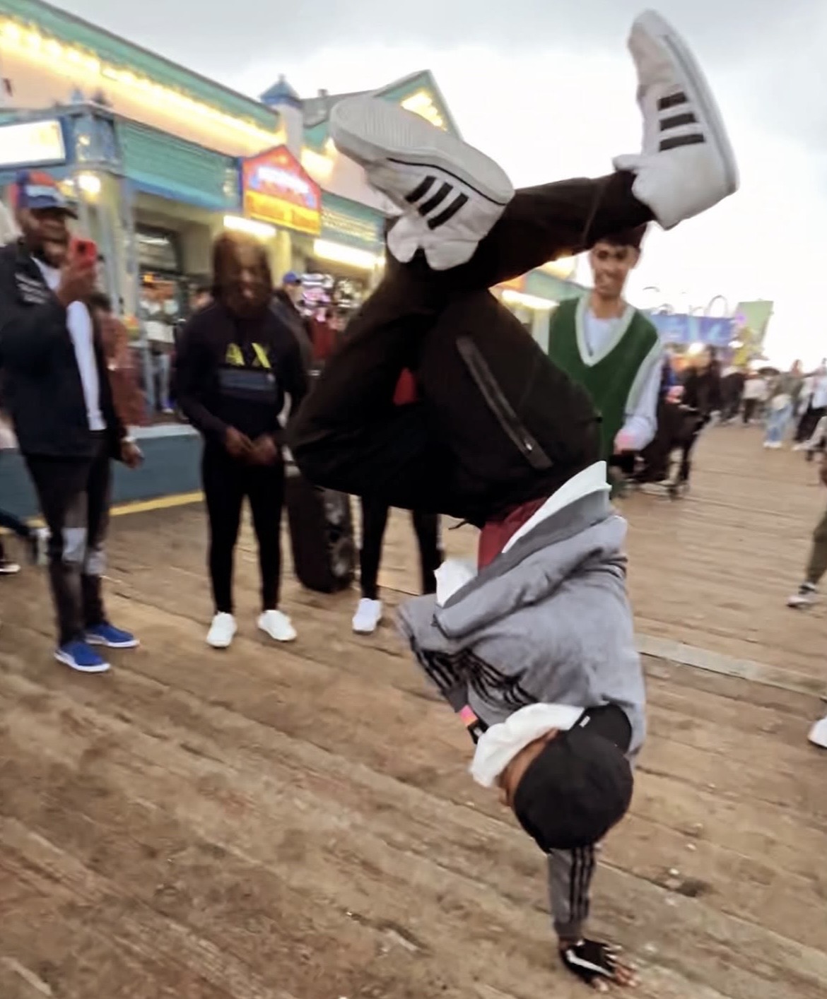 Person performing a headstand on a wooden boardwalk with onlookers in the background.
