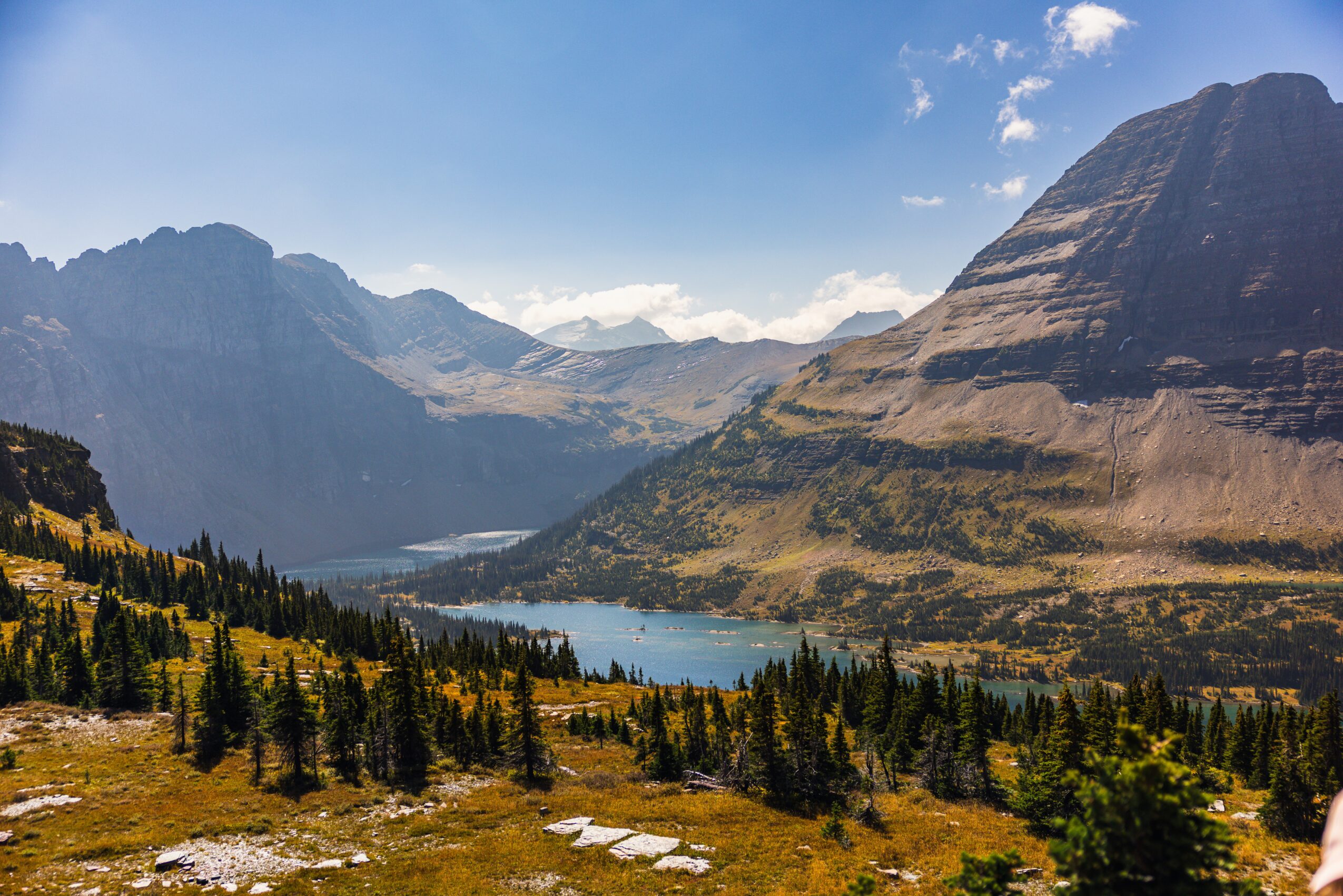 Mountain landscape with a lake, forest, and mountains under a partly cloudy sky.
