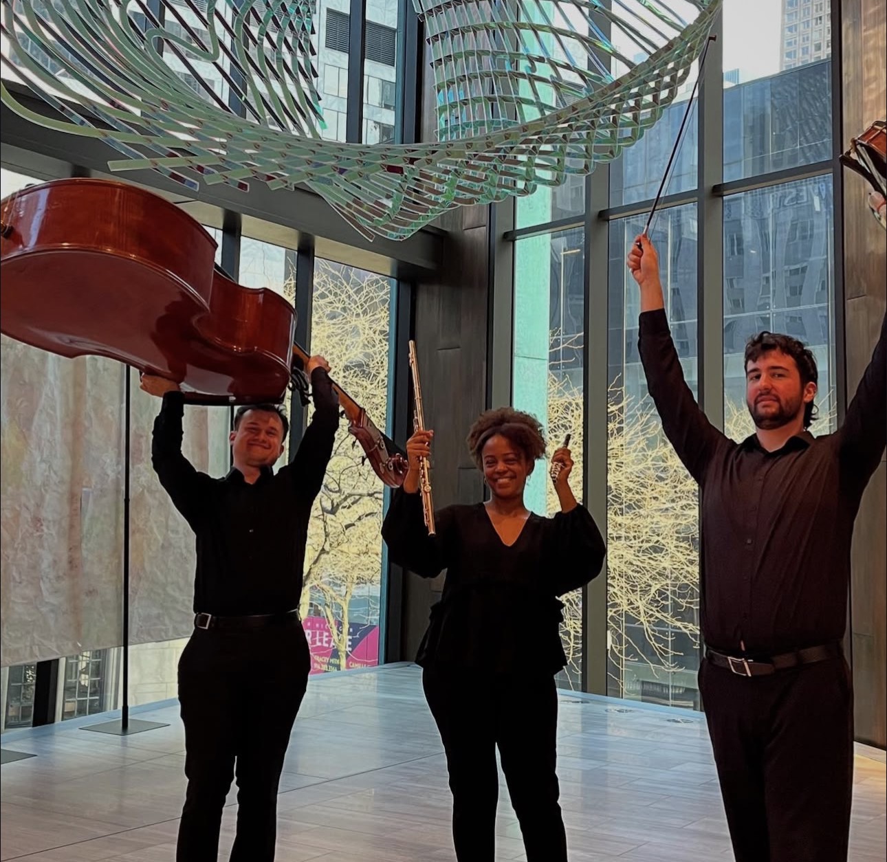 Three people holding a large red object inside a modern building with glass walls and tall windows.