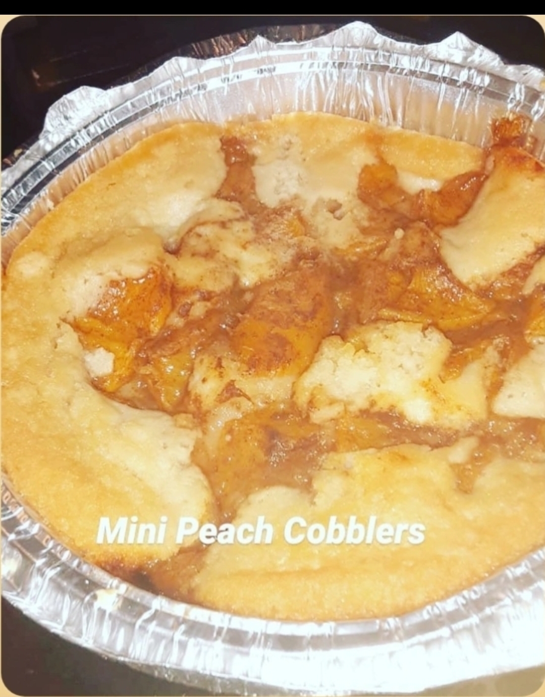 Mini peach cobbler in a foil container with peach filling and crust, labeled 'Mini Peach Cobblers'.