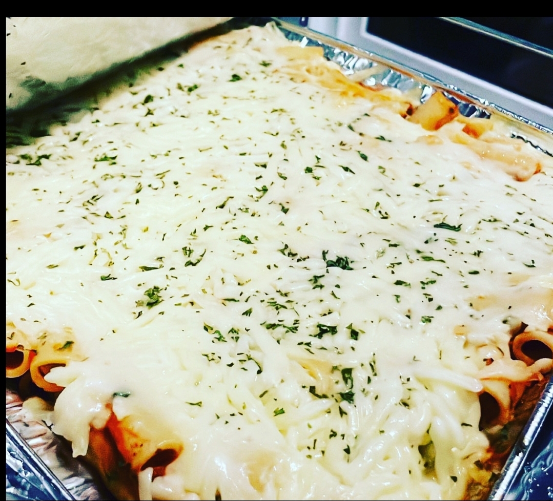 Baked pasta dish with melted cheese and herbs in a metal tray, viewed from above.