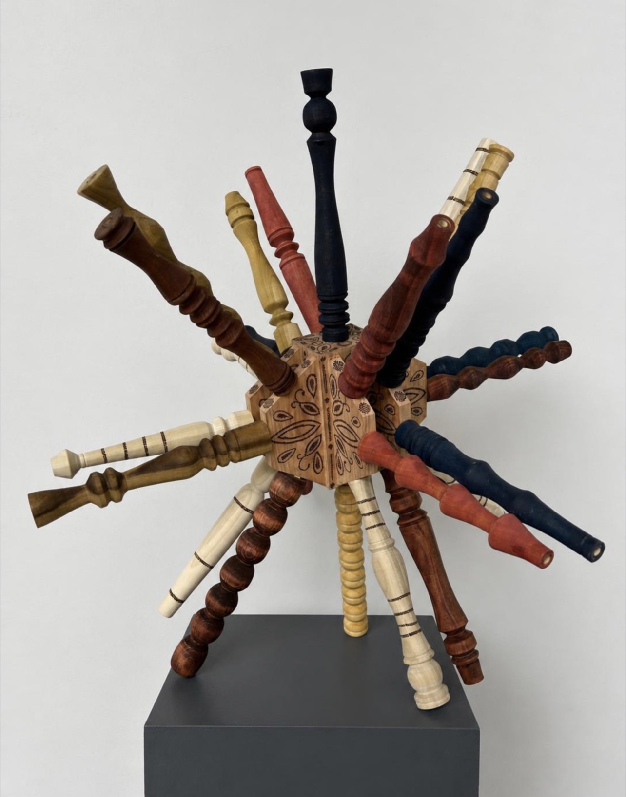 Multiple colorful wooden chairs arranged in a star shape on a gray pedestal against a white background.