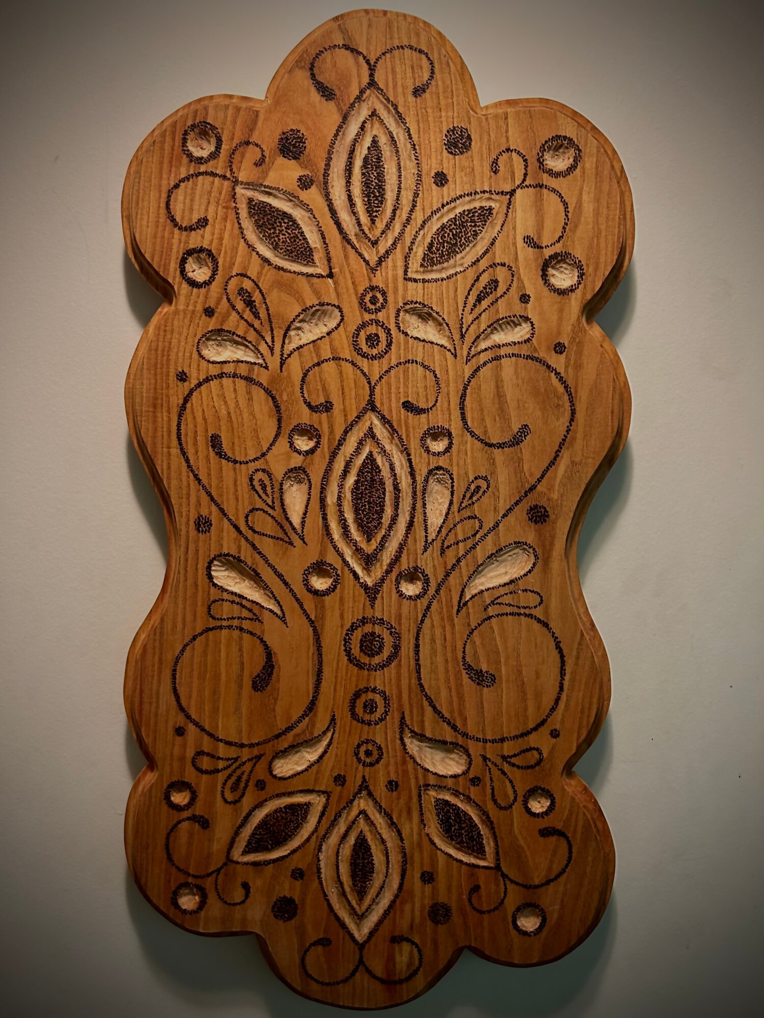 Decorative wooden piece with intricate black and white floral patterns and swirls, shaped with rounded edges.